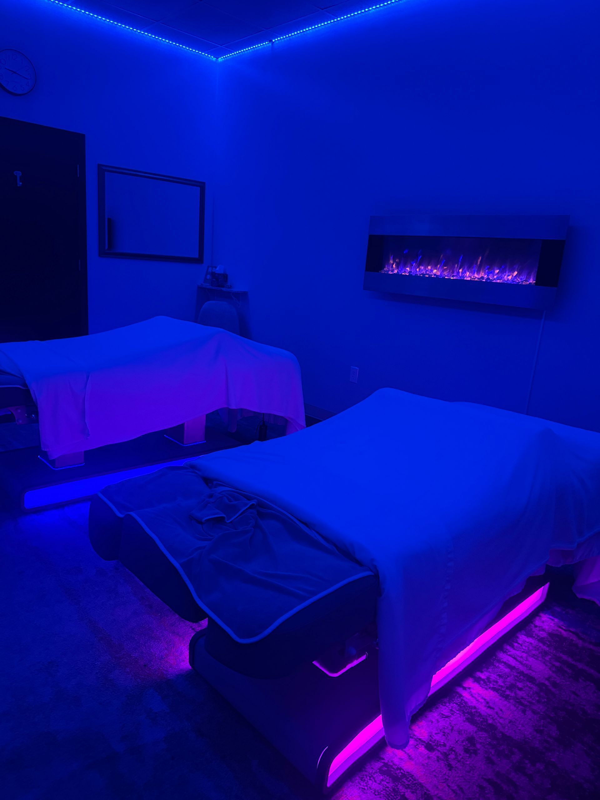 Blue-lit bedroom with two beds, purple LED accents, and a wall-mounted electric fireplace.