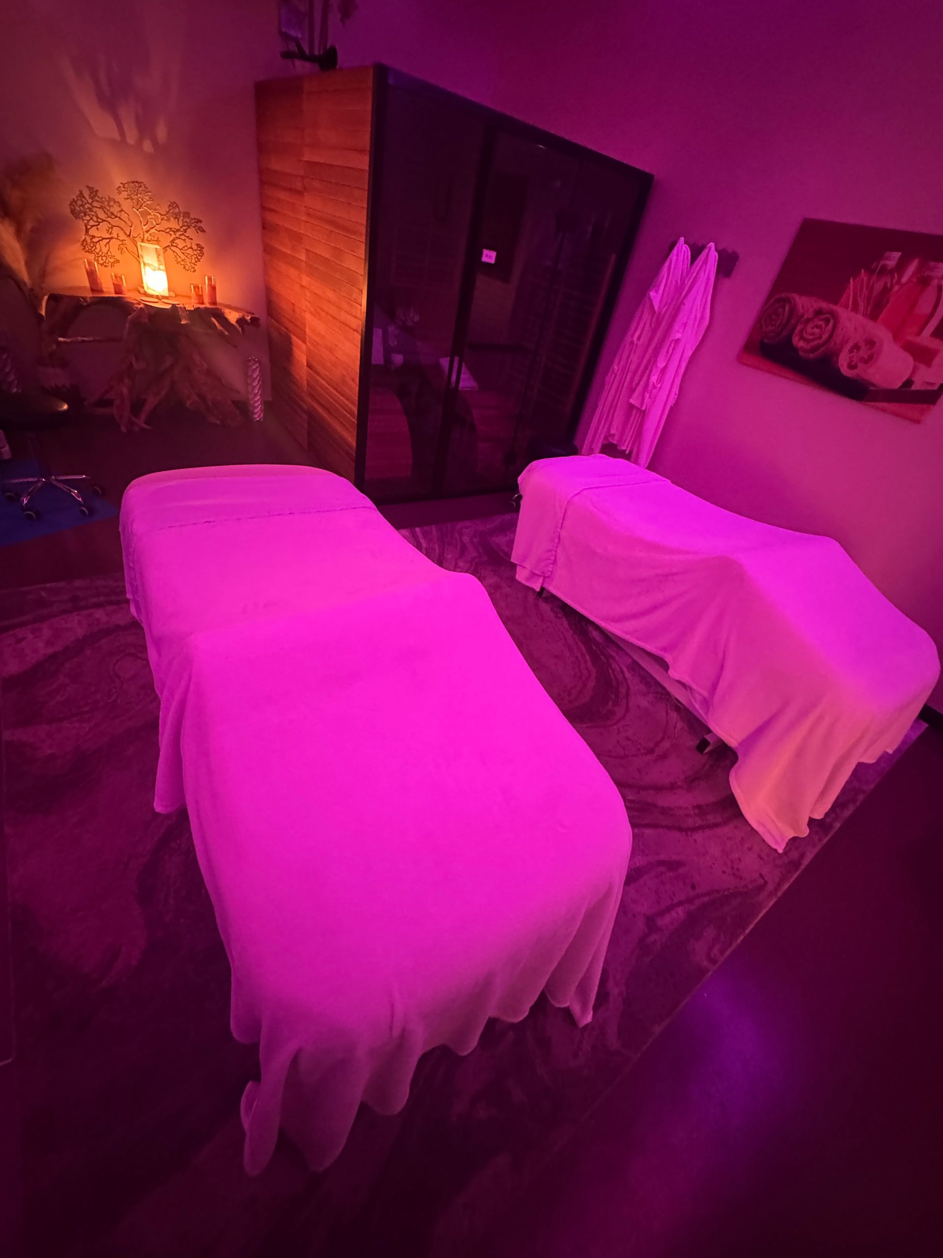 Spa room with two covered massage tables lit in pink and purple light.