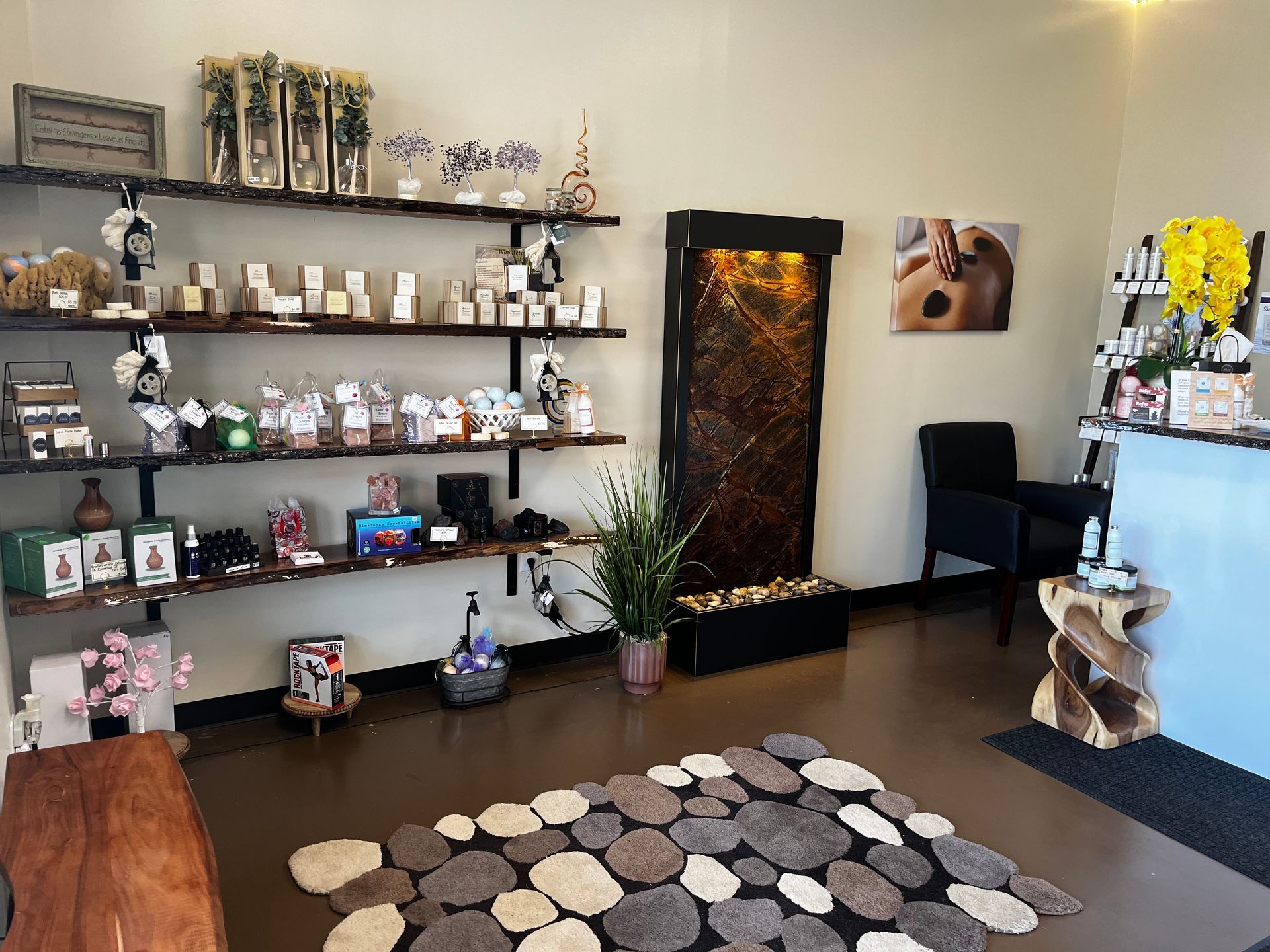 Modern living room with shelves of decor, a stone-pattern rug, potted plant, and black chair near a waterfall feature