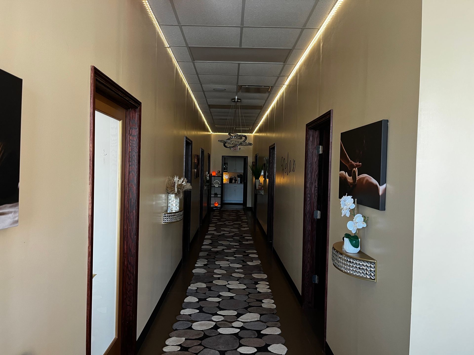 Narrow hallway with patterned carpet, beige walls, ceiling lights, and framed wall decor.