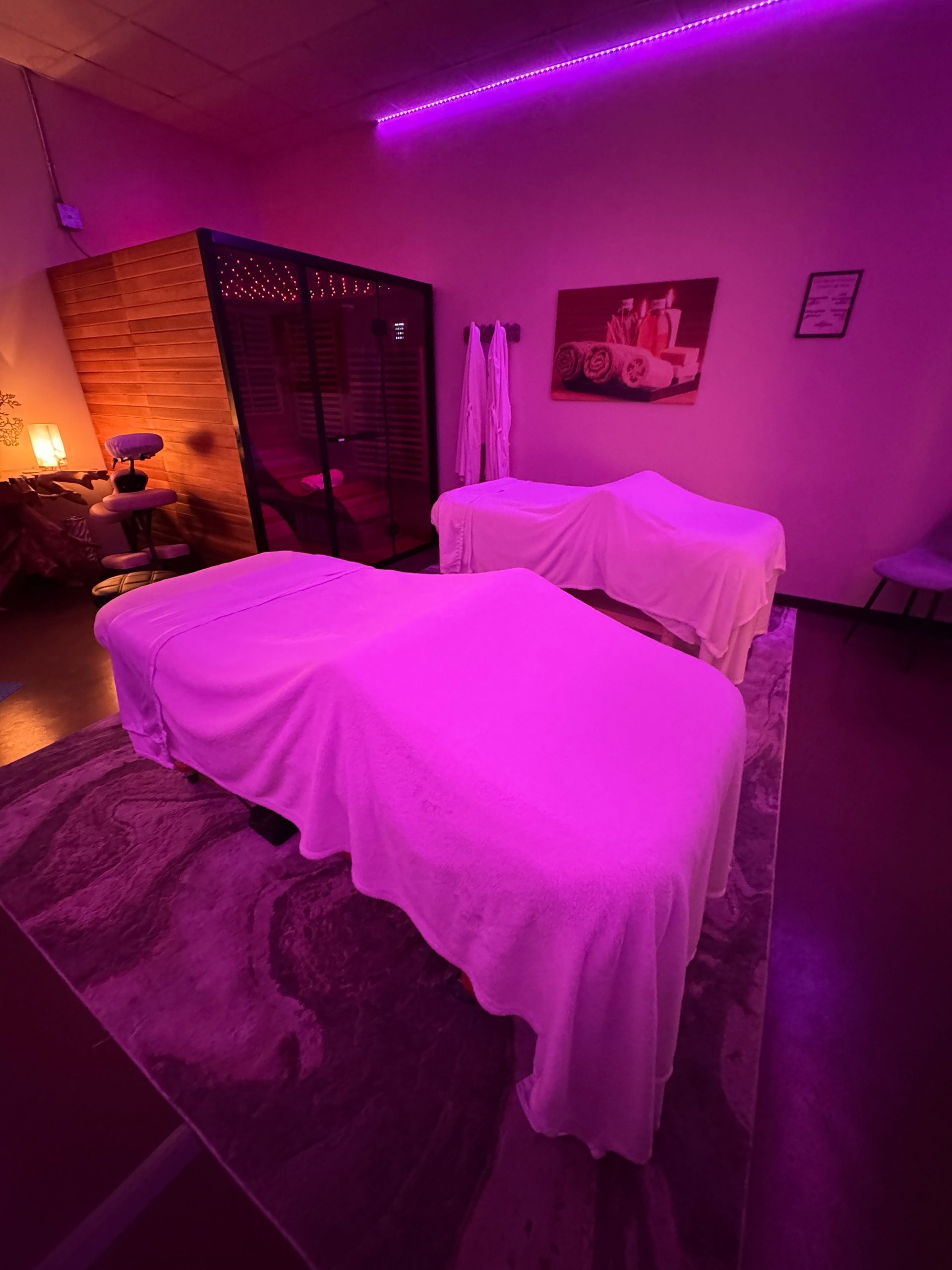 Purple-lit spa room with two massage tables covered in white sheets and towels