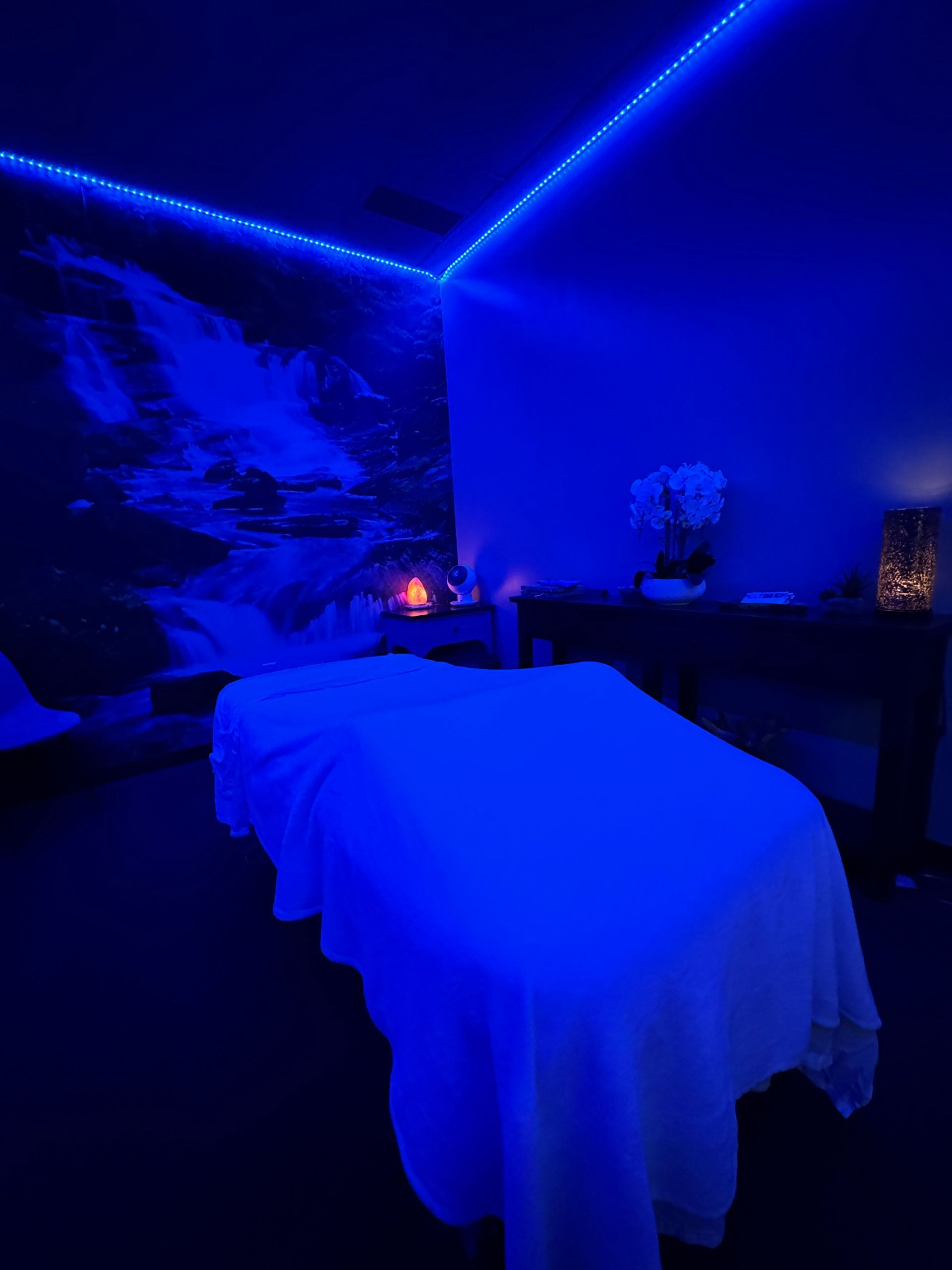 Blue-lit massage room with two treatment tables, candles, and a wall mural