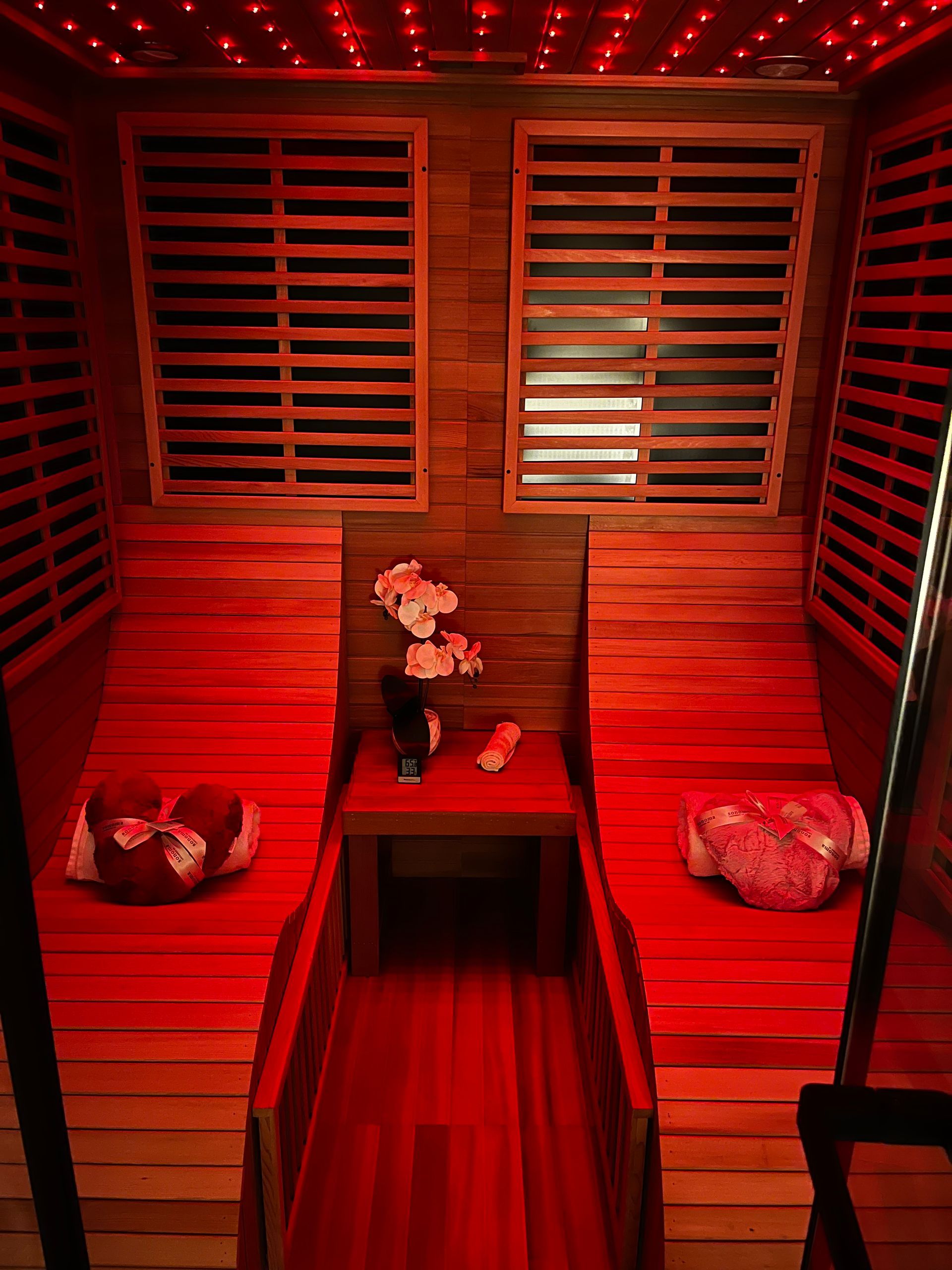 Red-lit wooden sauna with a person sitting on a bench and towels on the side benches
