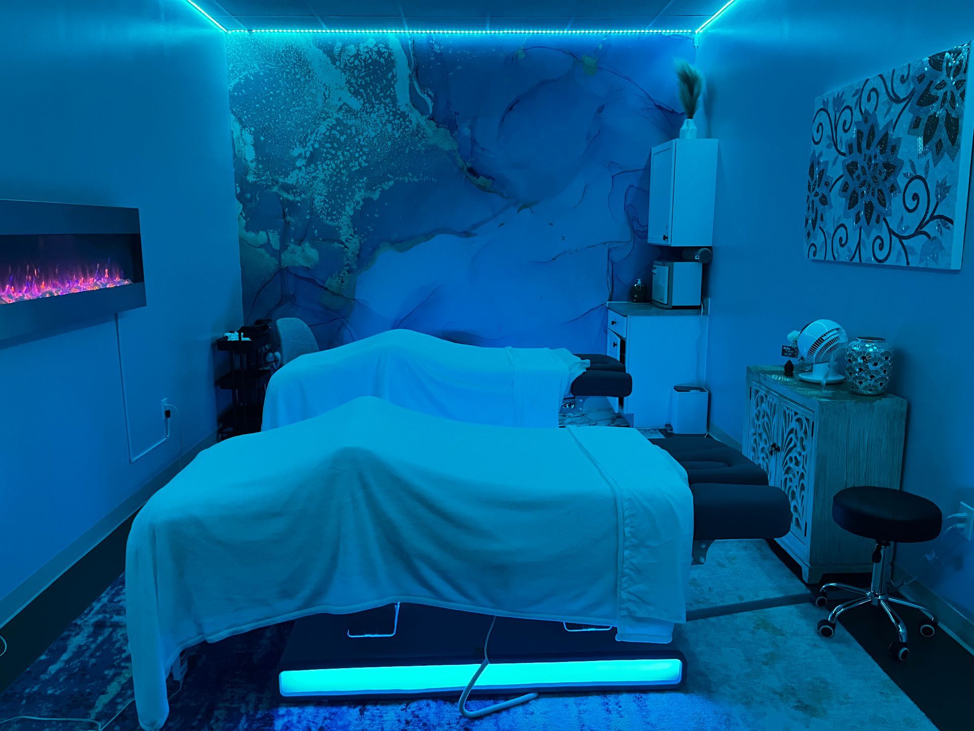 Blue-lit massage room with a treatment bed, wall decor, and spa equipment