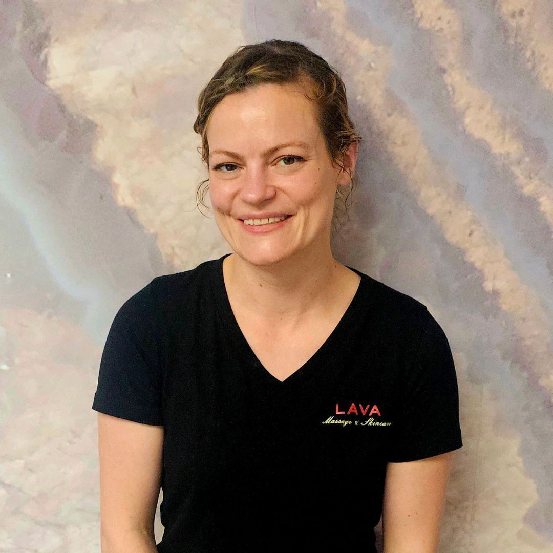 Smiling person in a black V-neck shirt against a soft cloudy backdrop