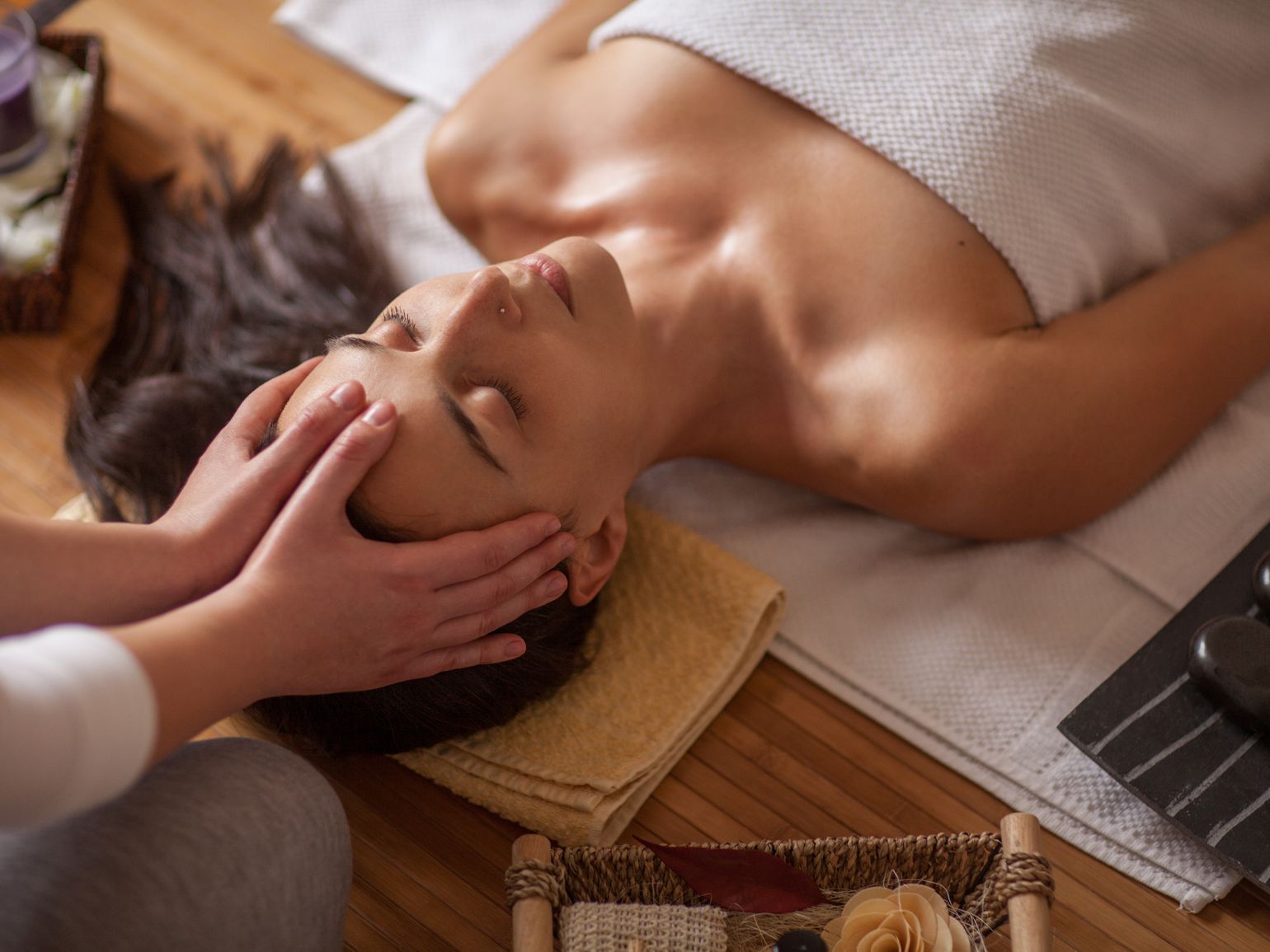 Person receiving a facial massage on a towel-covered spa table, with candles and a tray nearby