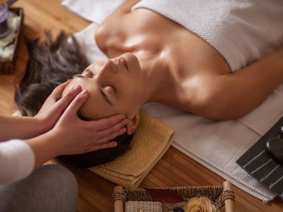 Person receiving a facial massage on a towel-covered spa table, with candles and a tray nearby