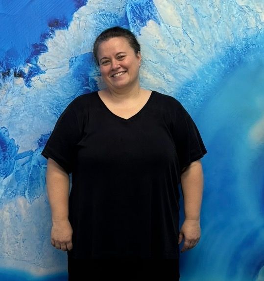 Smiling person in a black dress standing before a blue abstract background