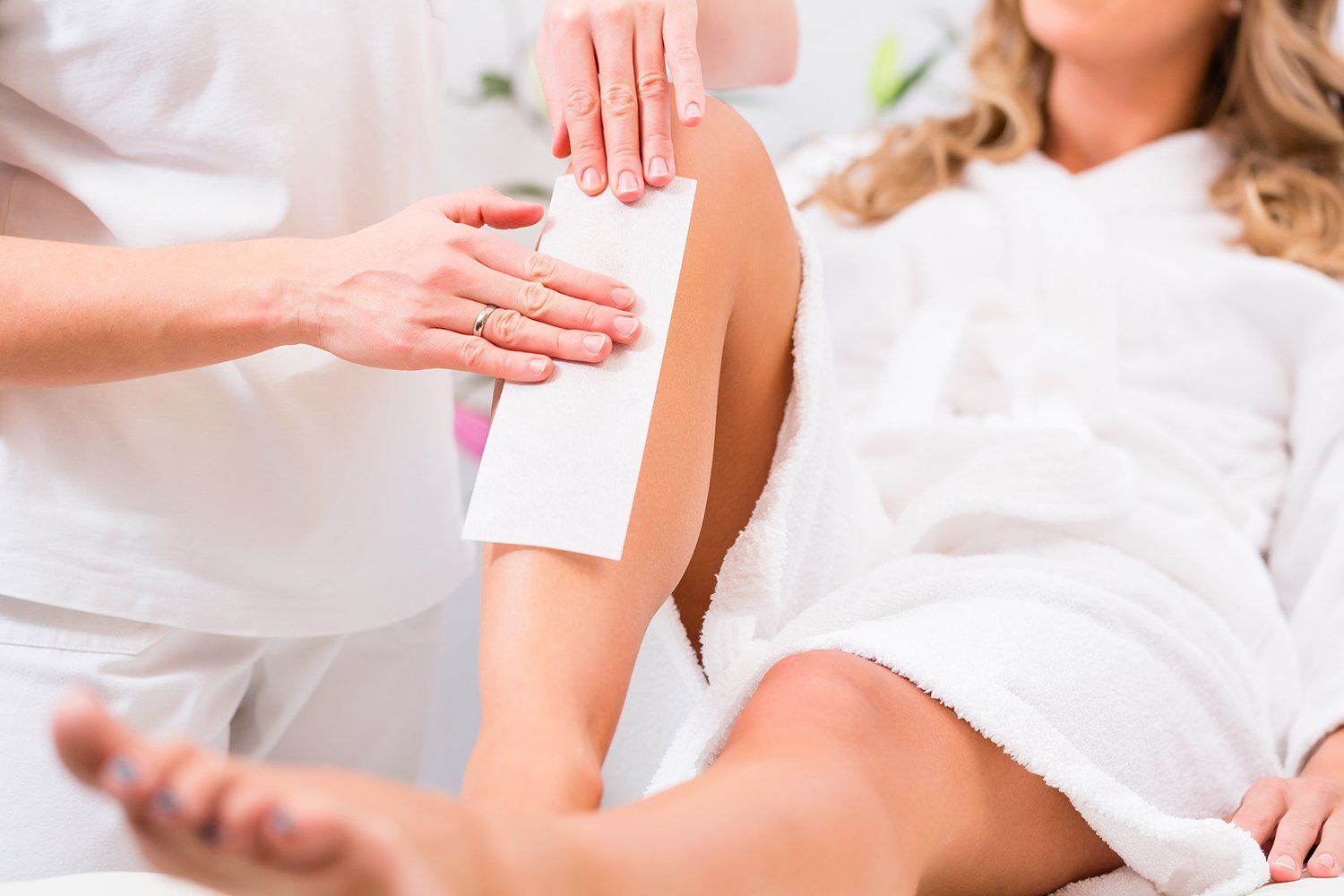 Person applying a white wax strip to a client’s upper arm during a beauty treatment