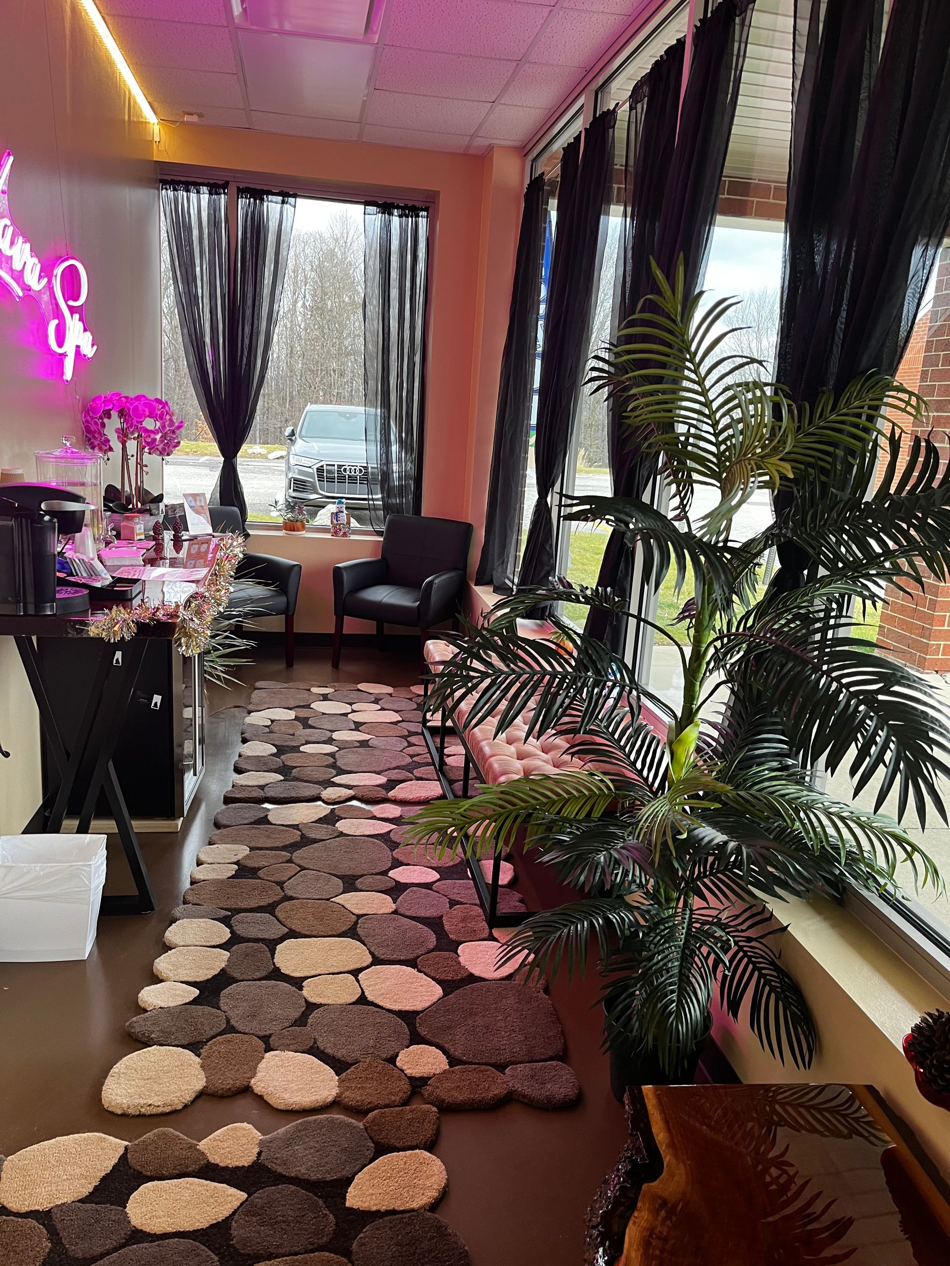 Cozy living room with patterned rug, plants, black curtains, and pink neon wall light by a window