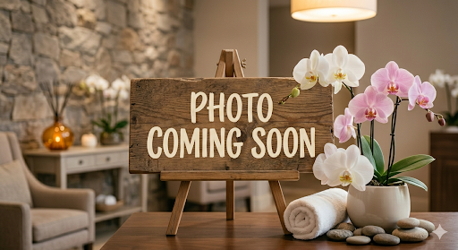 Wooden sign reading “PHOTO COMING SOON” on a cozy spa-like table with orchids and rolled towels