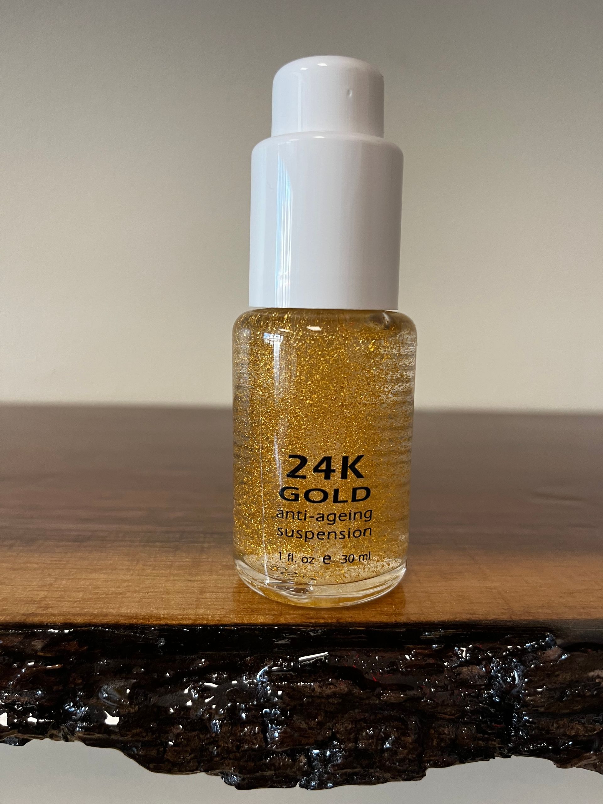 Small bottle of 24K gold glitter nail polish on a wooden surface.