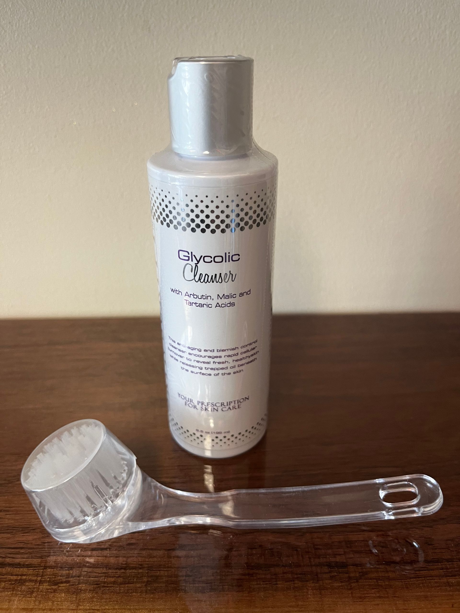Silver cosmetic bottle with a clear plastic applicator cap lying in front on a beige surface