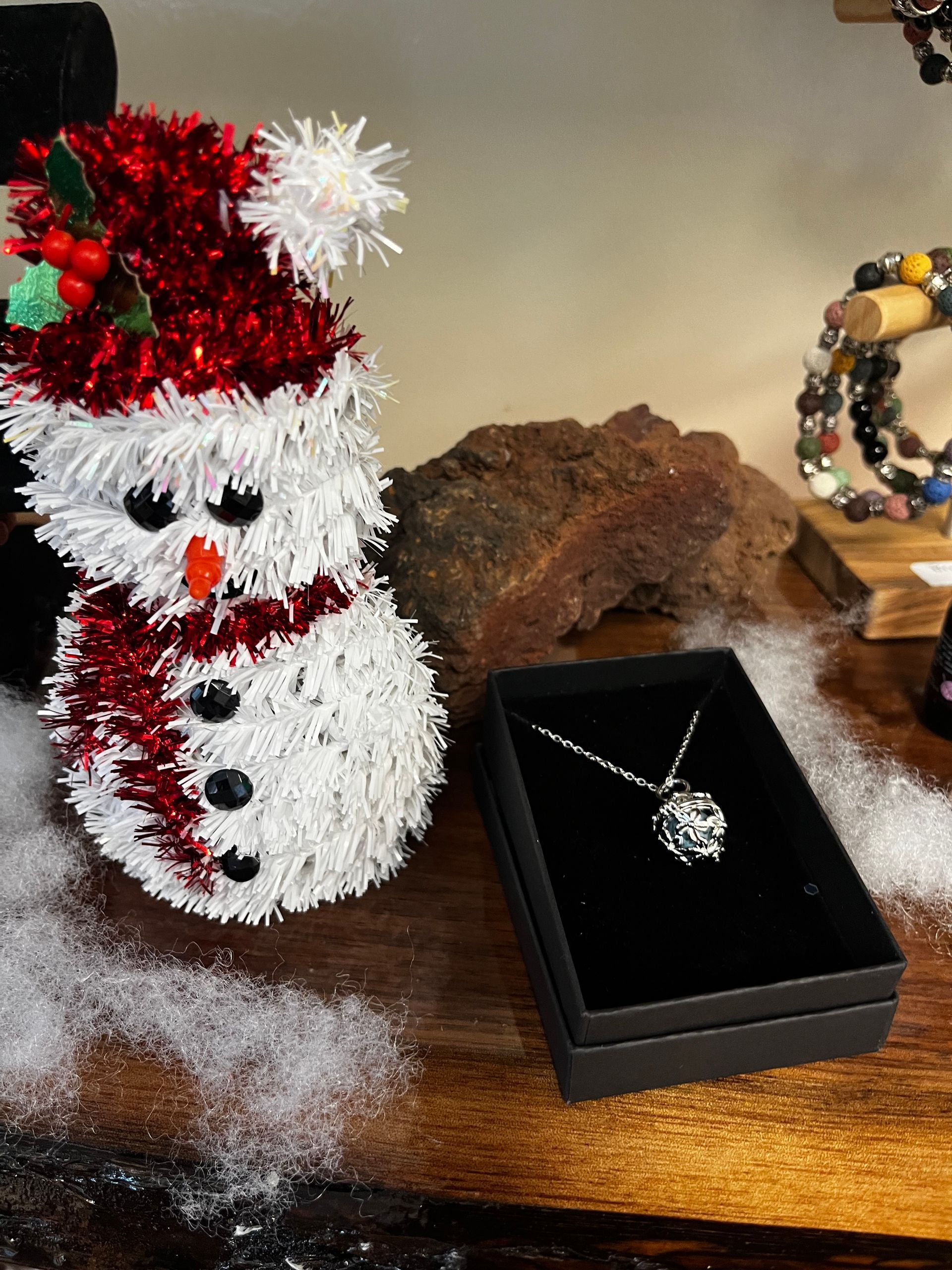 Snowman decoration beside a black jewelry box with a silver necklace on a wooden table