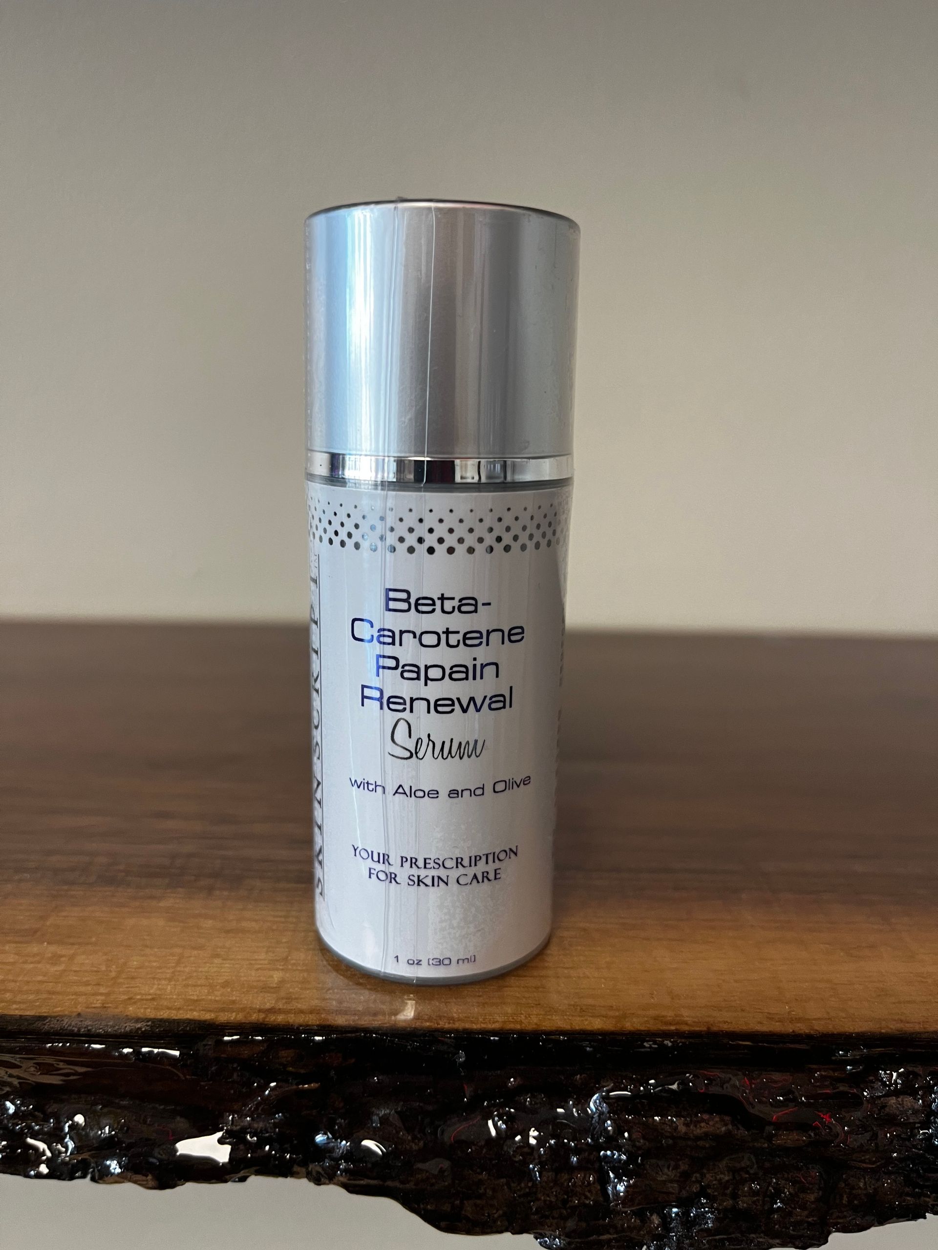 Silver cosmetic bottle on a wooden surface against a beige wall.