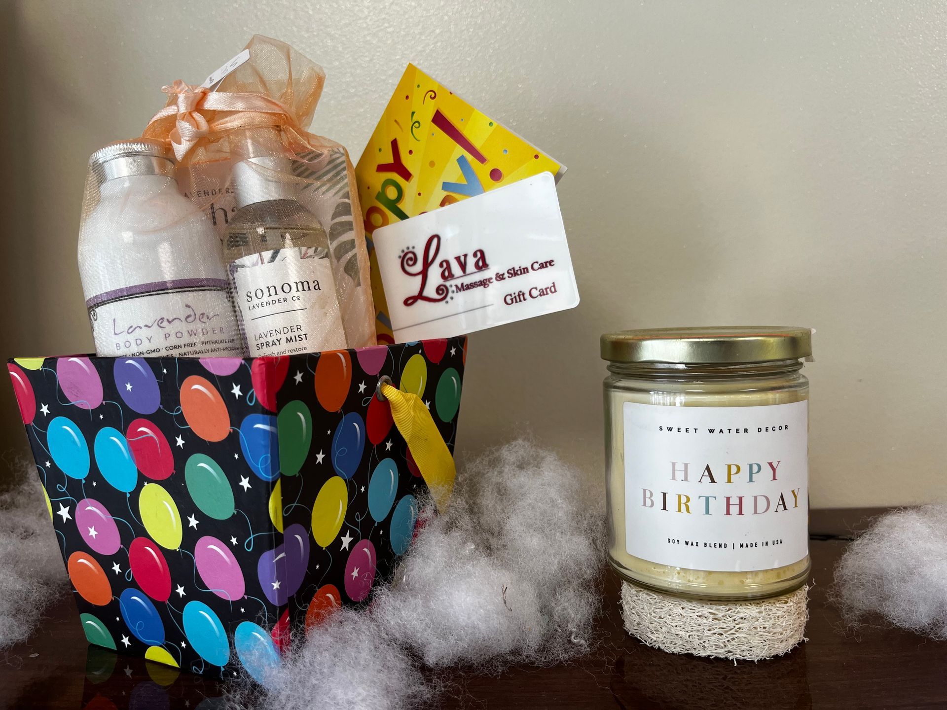 Gift basket with colorful polka-dot wrapper, treats, and a “Happy Birthday” candle on a table