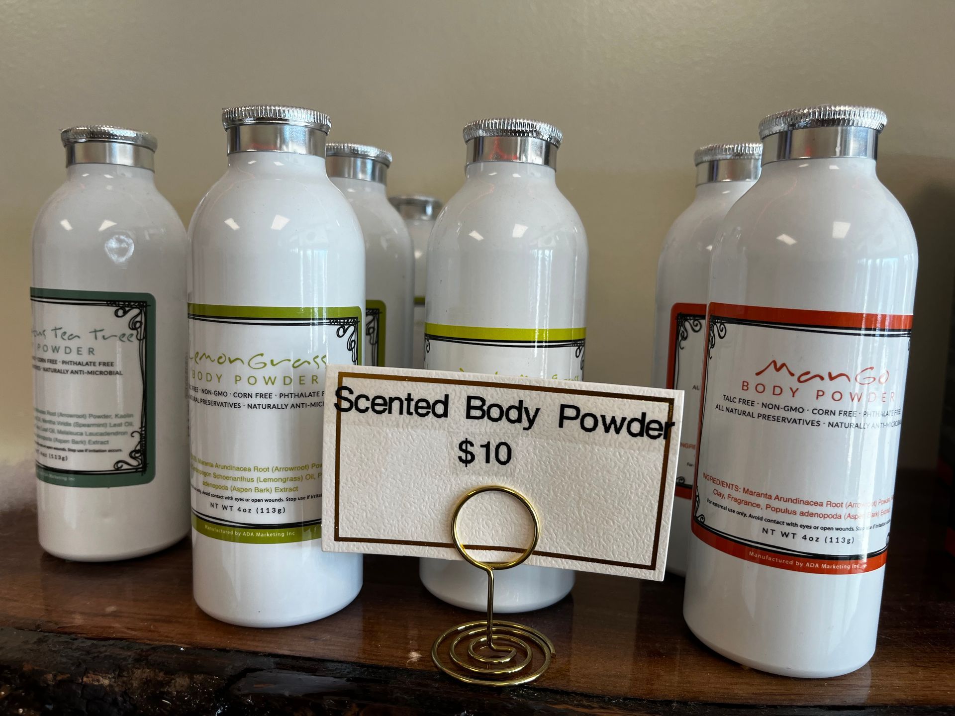 Four white bottles behind a sign reading “Scented Body Powder $10”