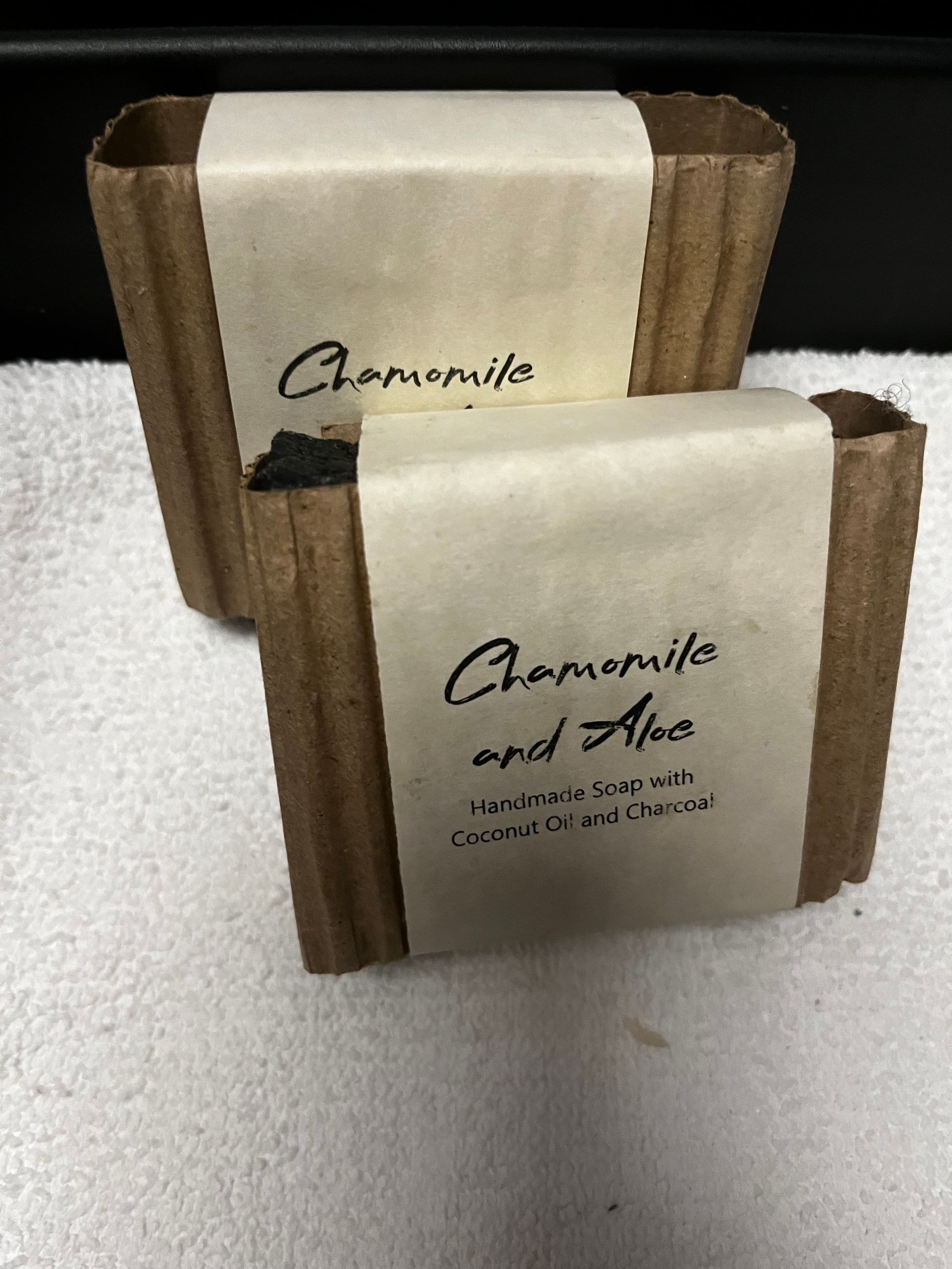Two chamomile soap bars in brown and cream paper wrappers on a white surface.