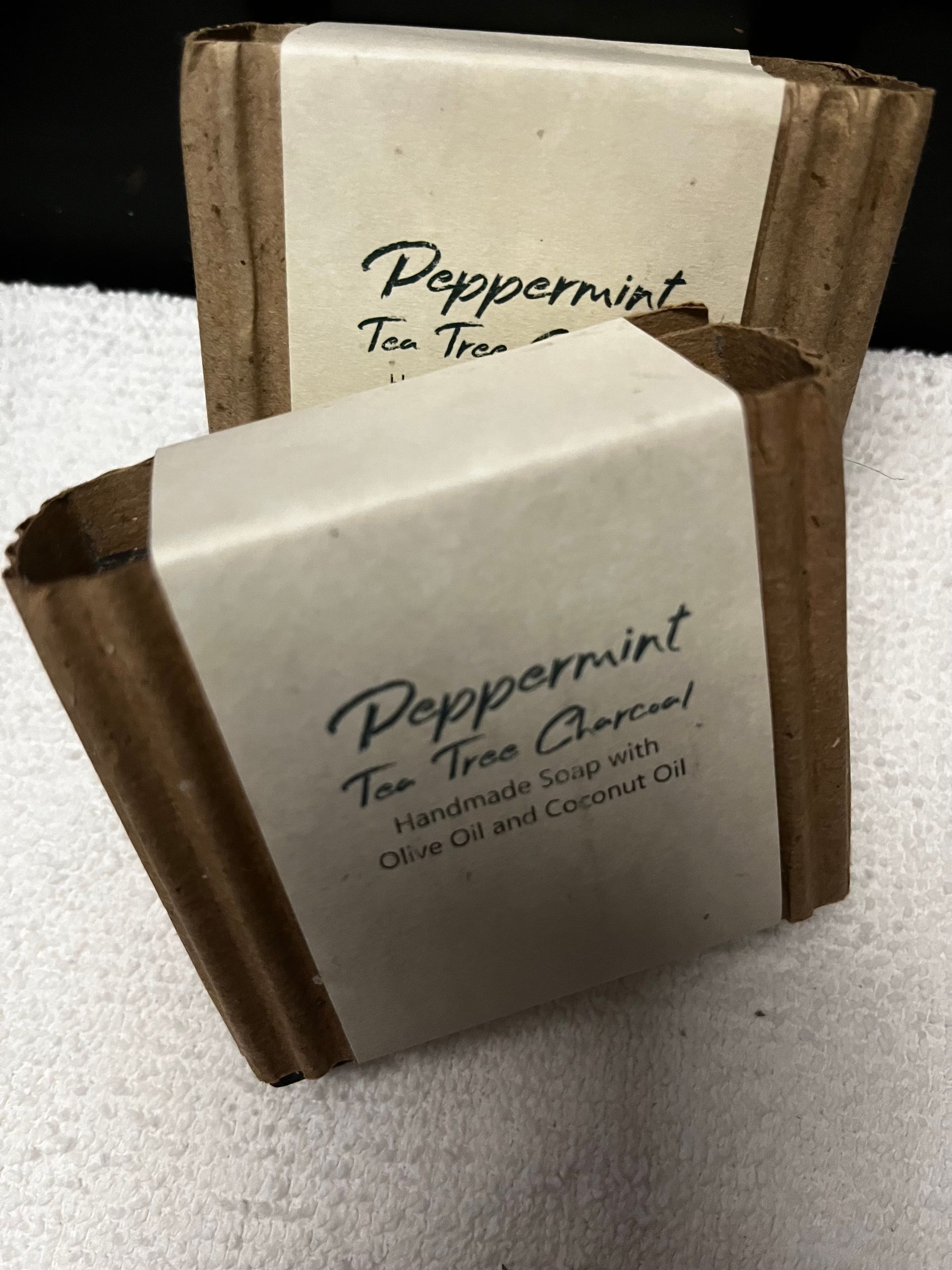 Two peppermint tea soap bars wrapped in brown paper on a white towel