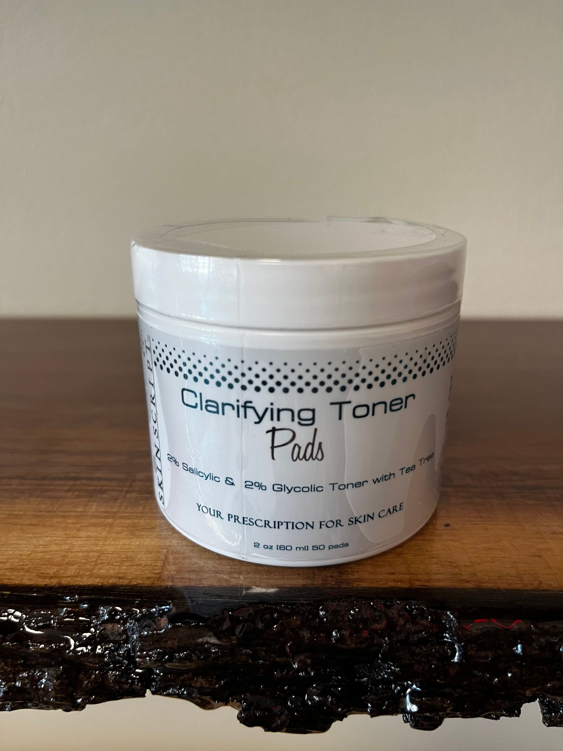 White jar of Clarifying Toner Pads on a wooden surface against a beige wall.