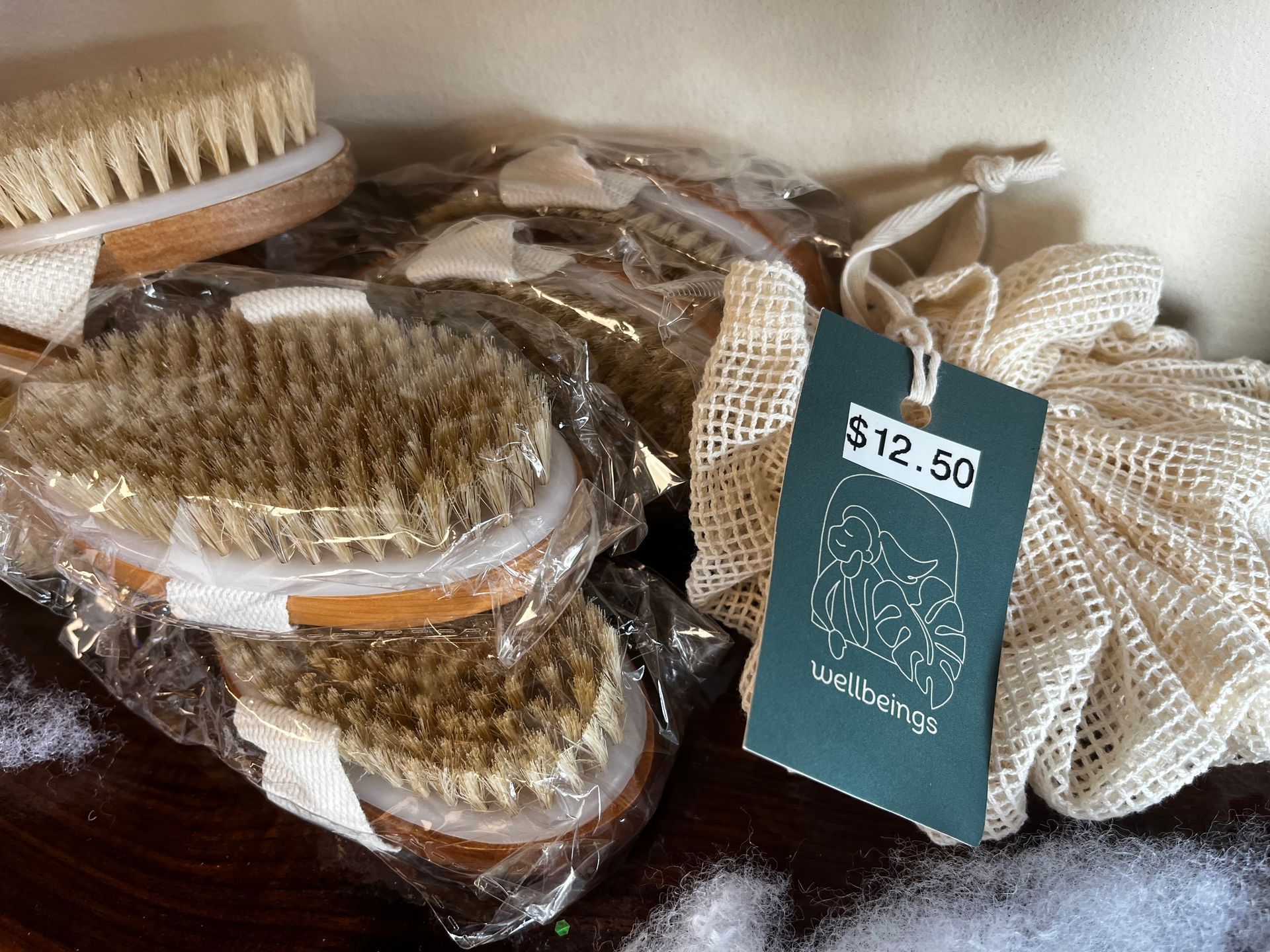 Assorted packaged bath brushes and loofahs on a table, with a $12.50 price tag.