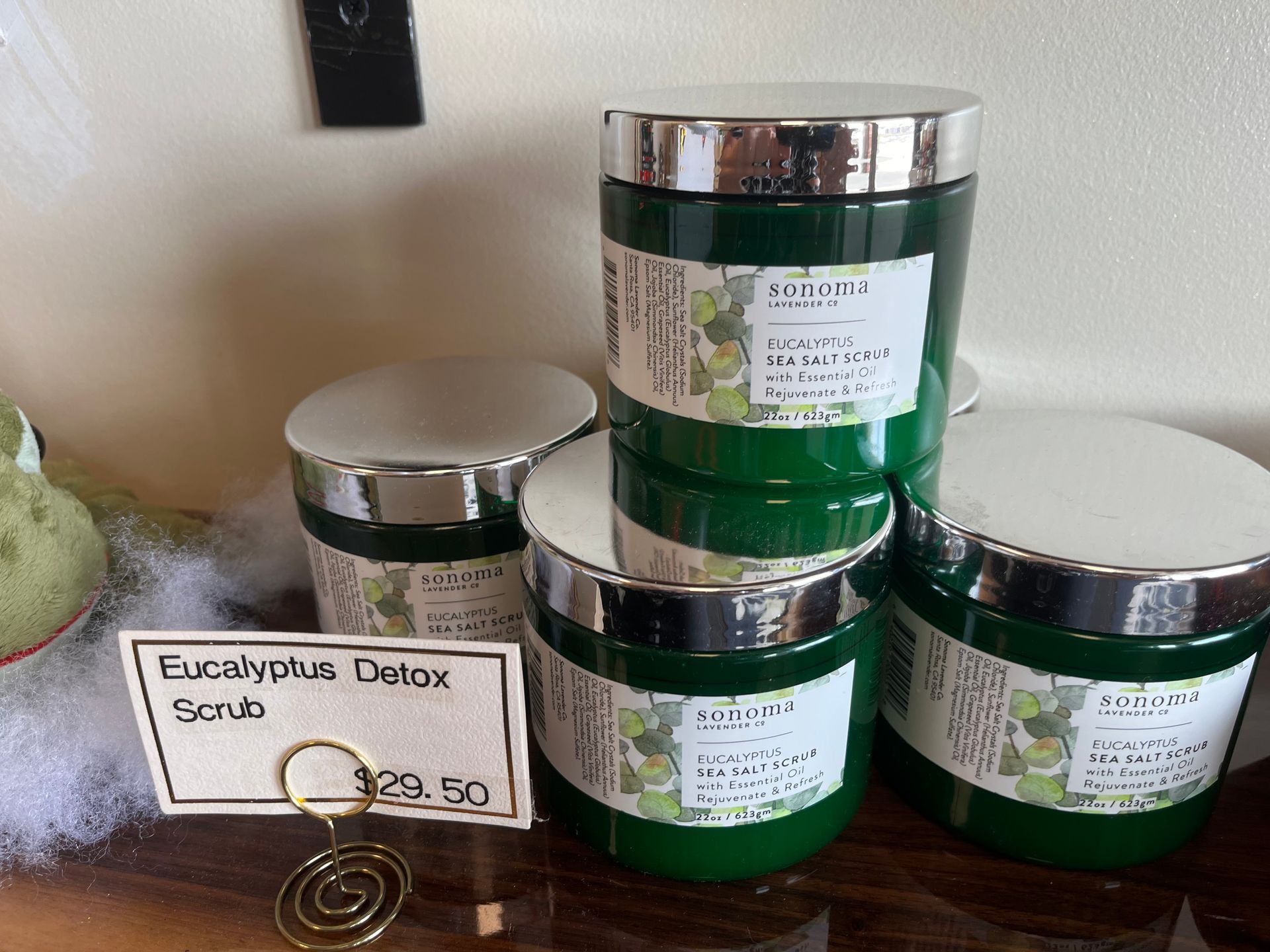 Green jars of eucalyptus detox scrub with silver lids on a shelf, beside a handwritten label.