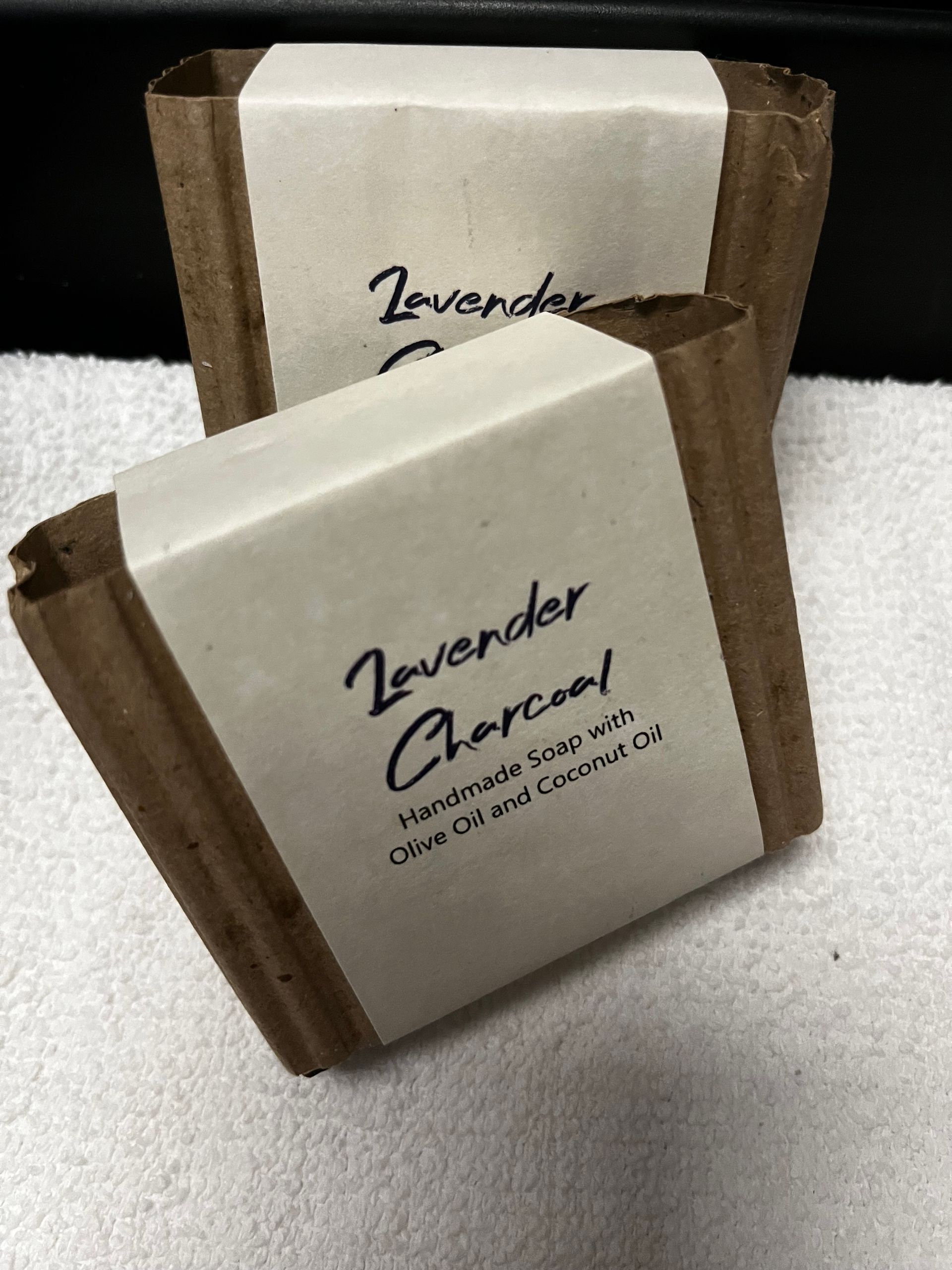 Two soap bars in white labels with brown cardboard sleeves on a light countertop.