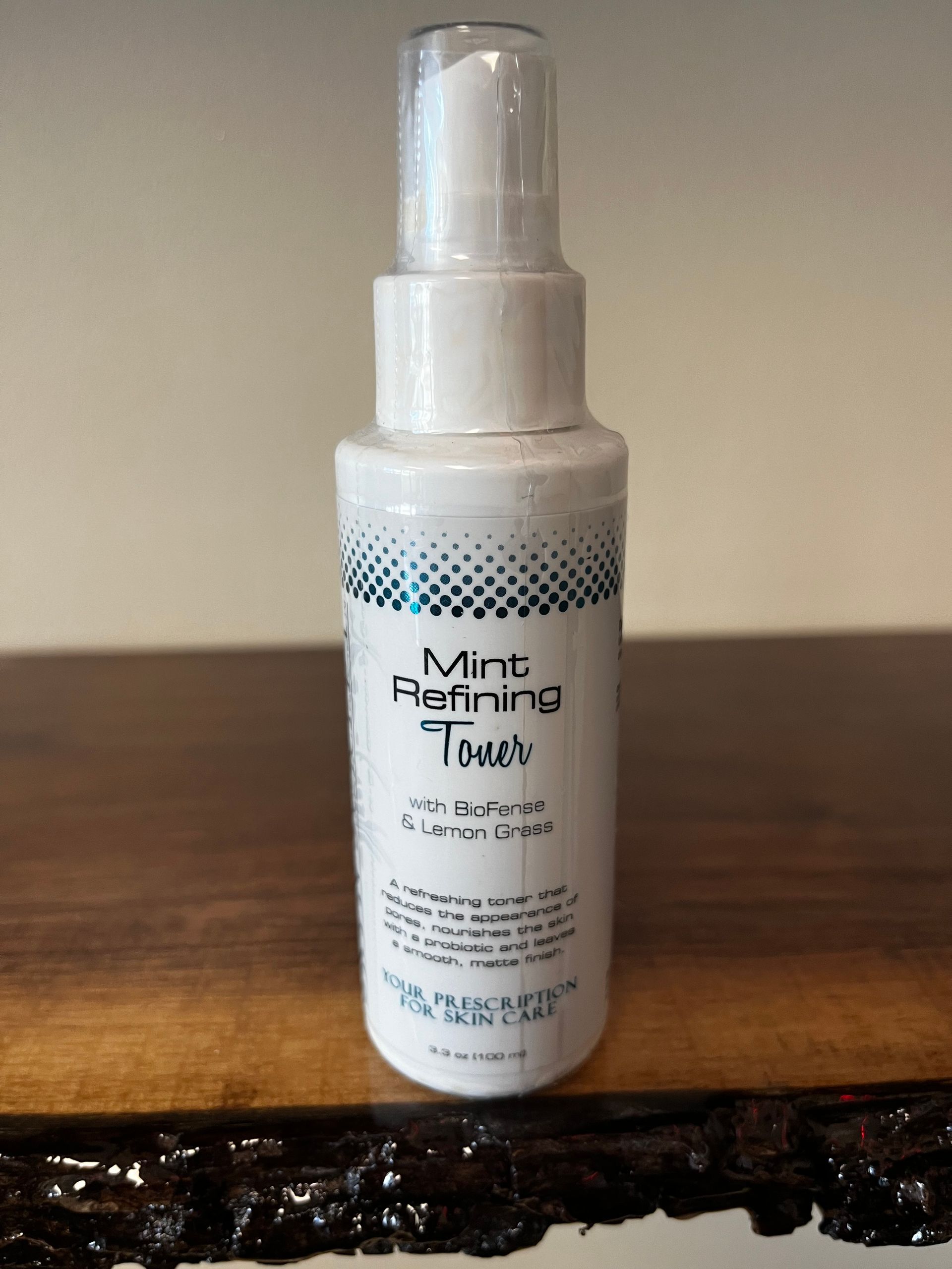 White bottle of mint refining tonic with a spray cap on a wooden surface.