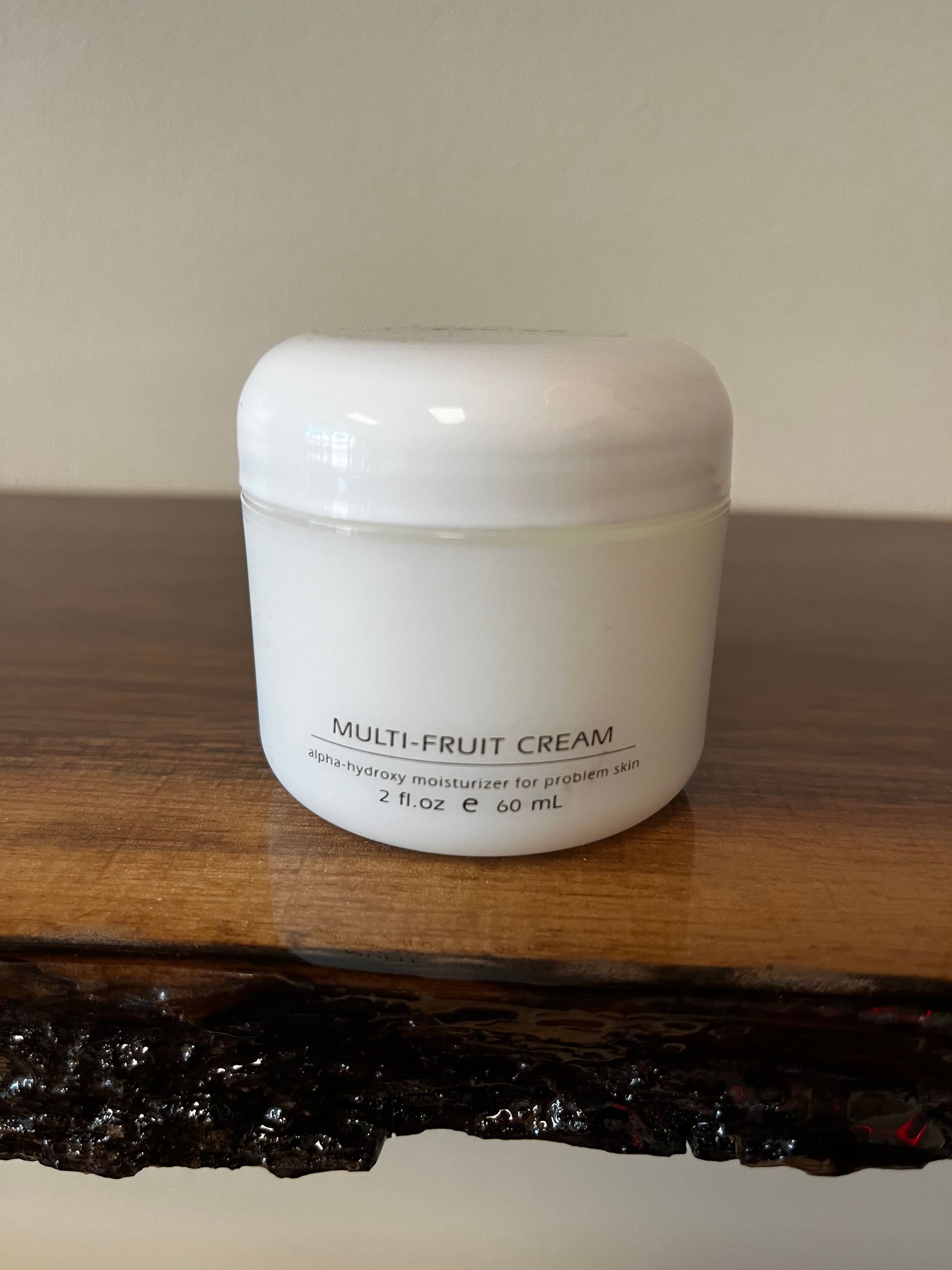 White skincare cream jar on a wooden shelf against a beige wall.
