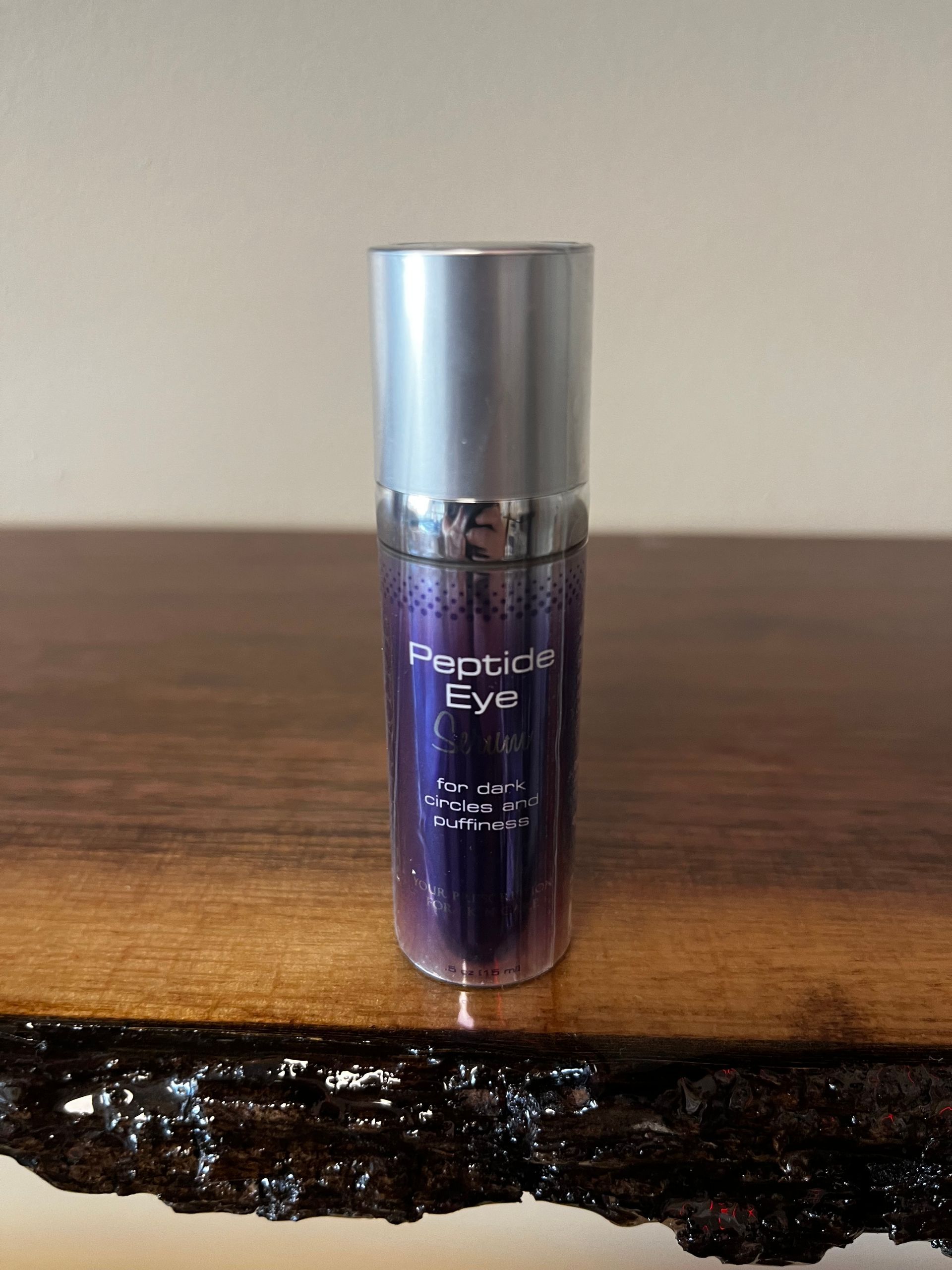 Purple cosmetic bottle with silver cap standing on a wooden table