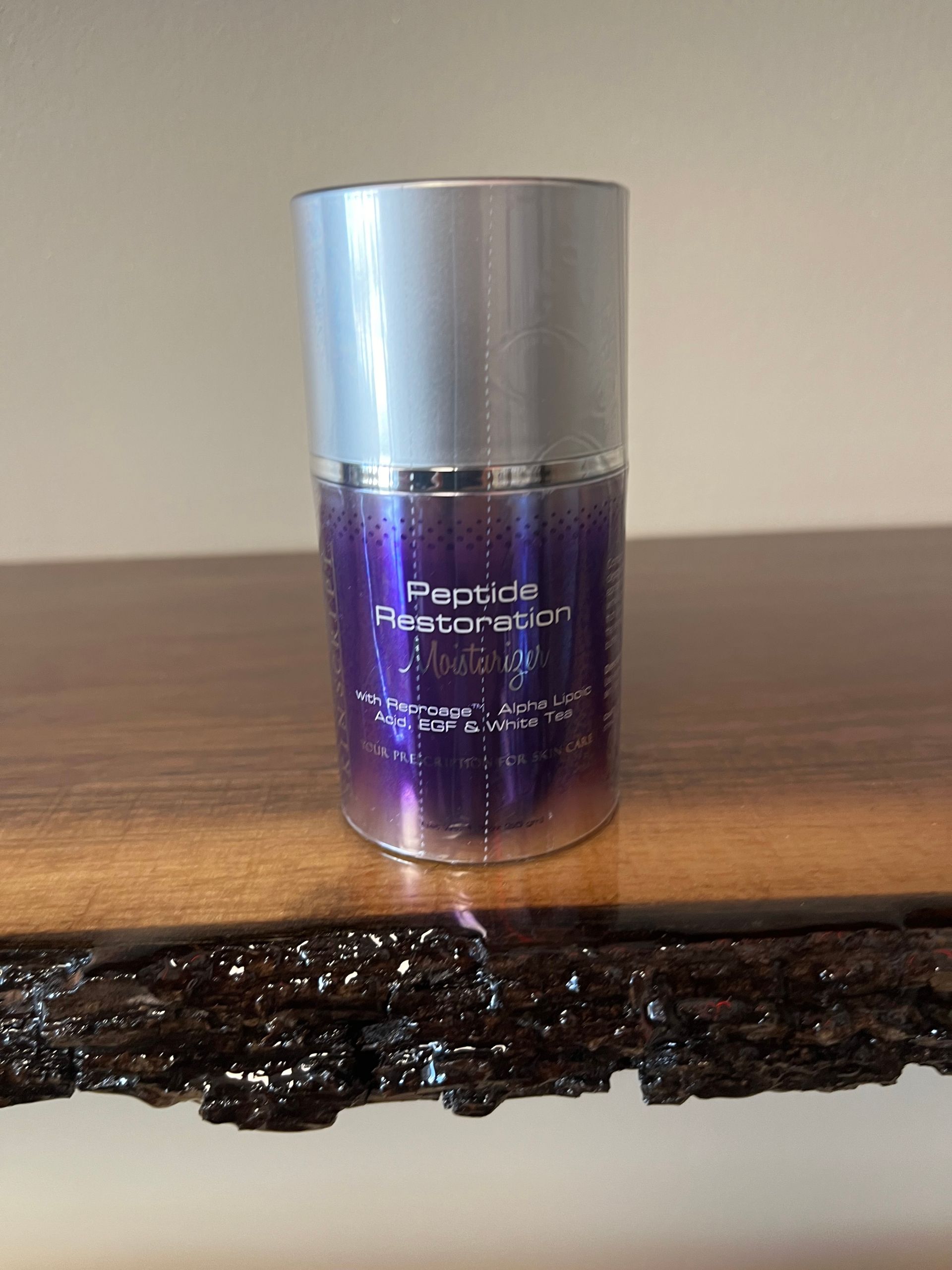 Purple cosmetic bottle with silver cap on a wooden surface, with dark melted debris in front