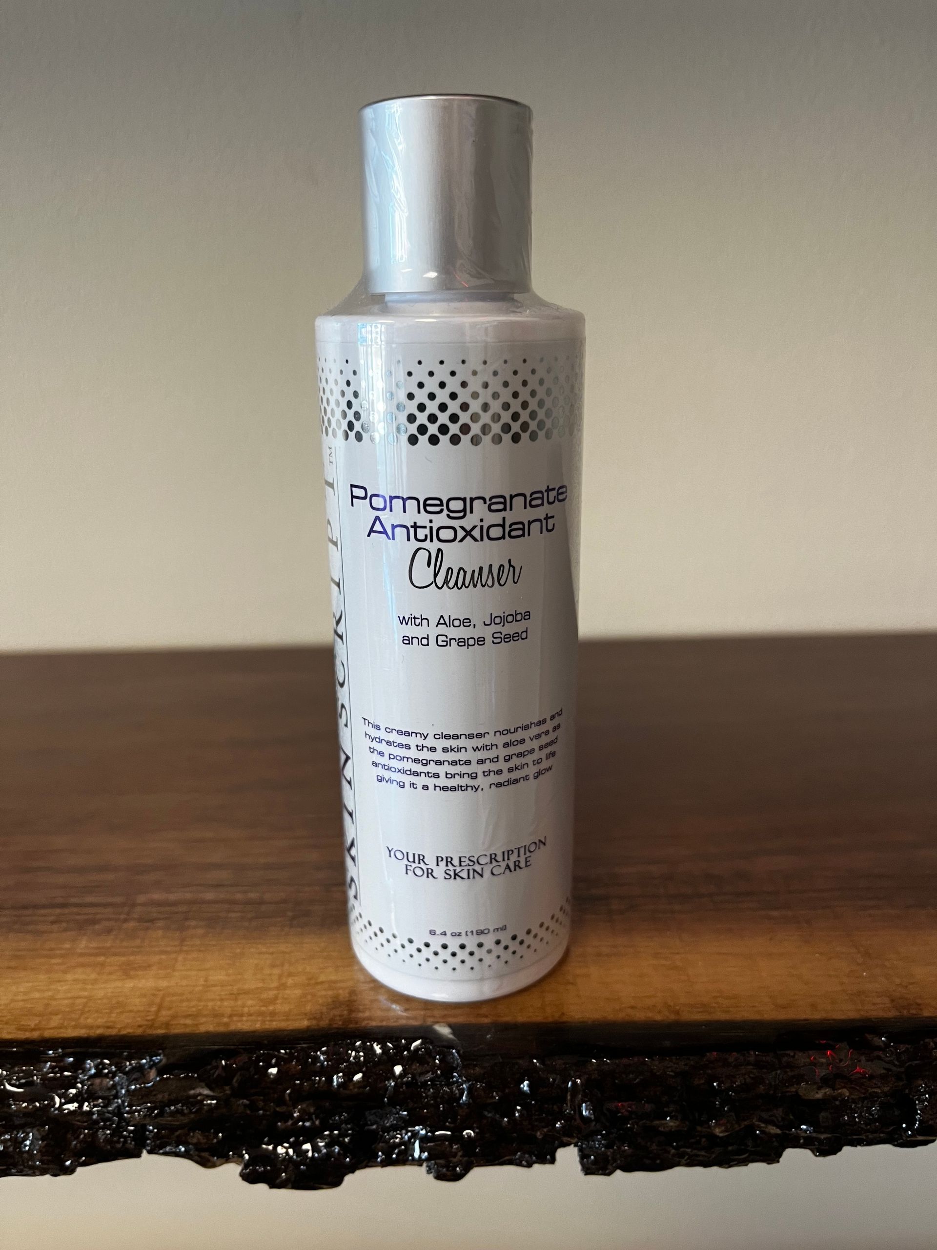 Silver bottle of Pomegranate Antioxidant Cleanser on a wooden table against a plain wall