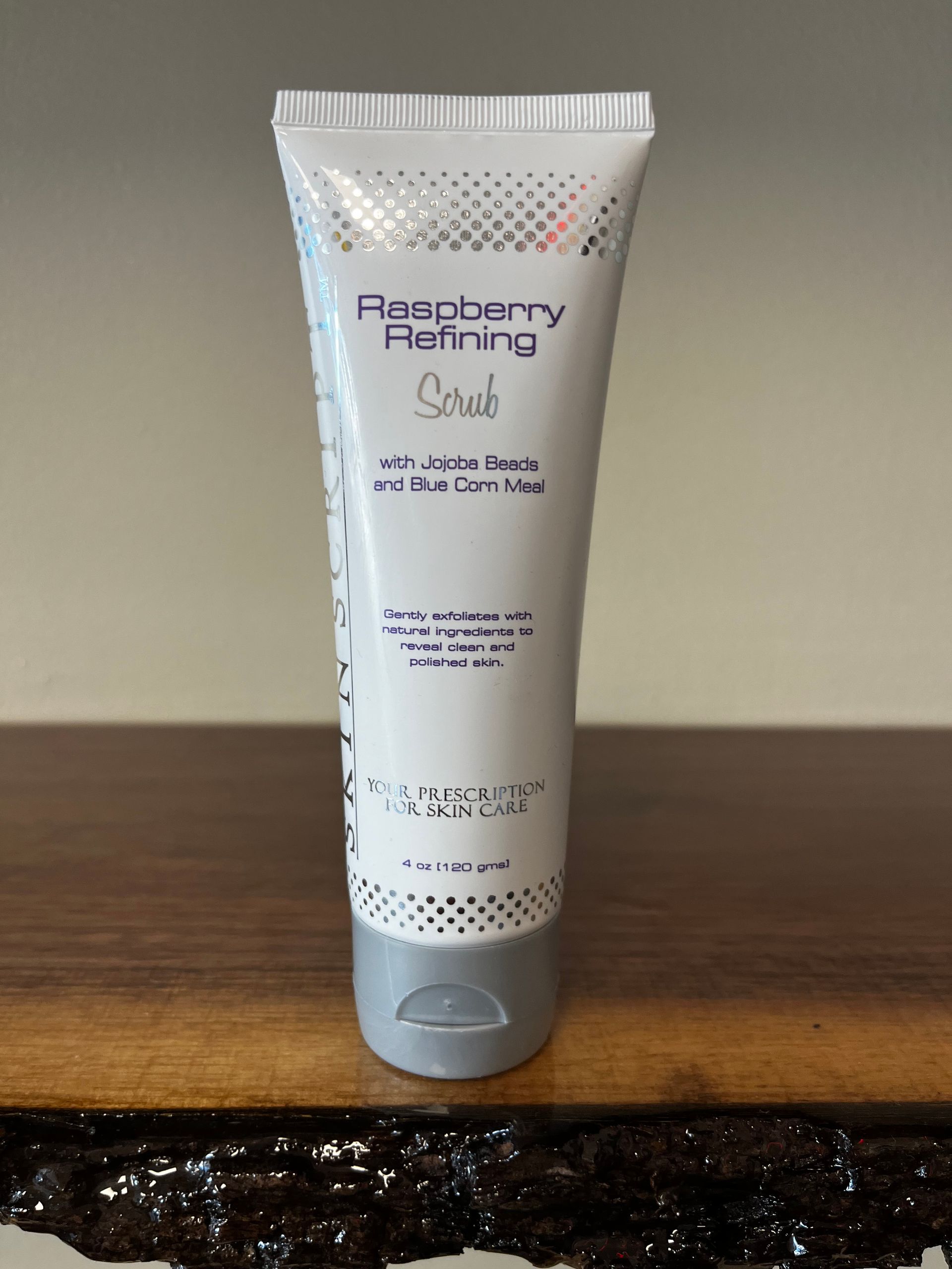White skincare tube labeled “Blackberry Refining Scrub” standing on a wooden surface.