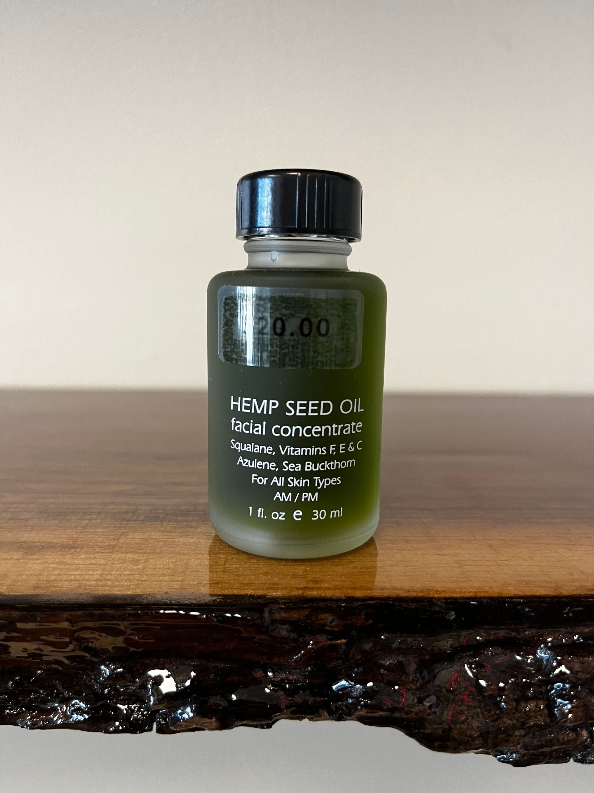 Small green bottle with a black cap sitting on a wooden surface against a plain wall.