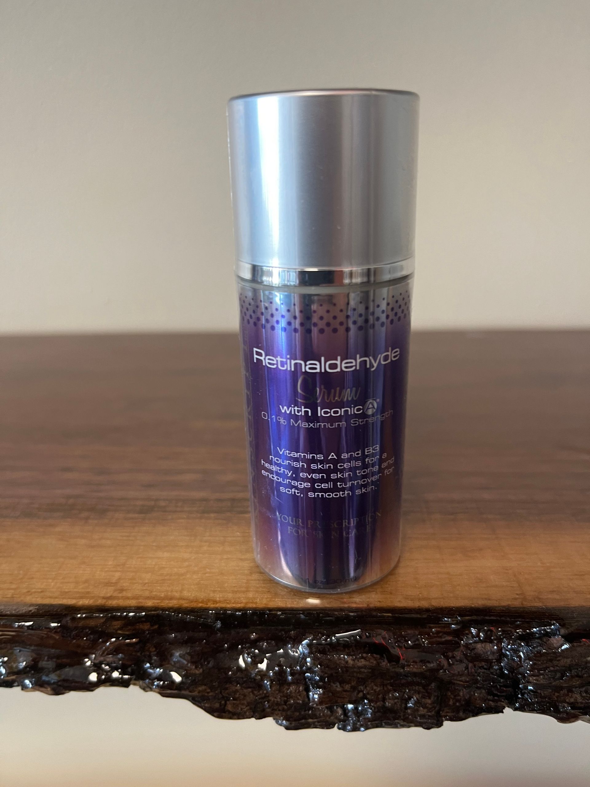 Purple cylindrical cosmetic bottle with silver cap on a wooden surface