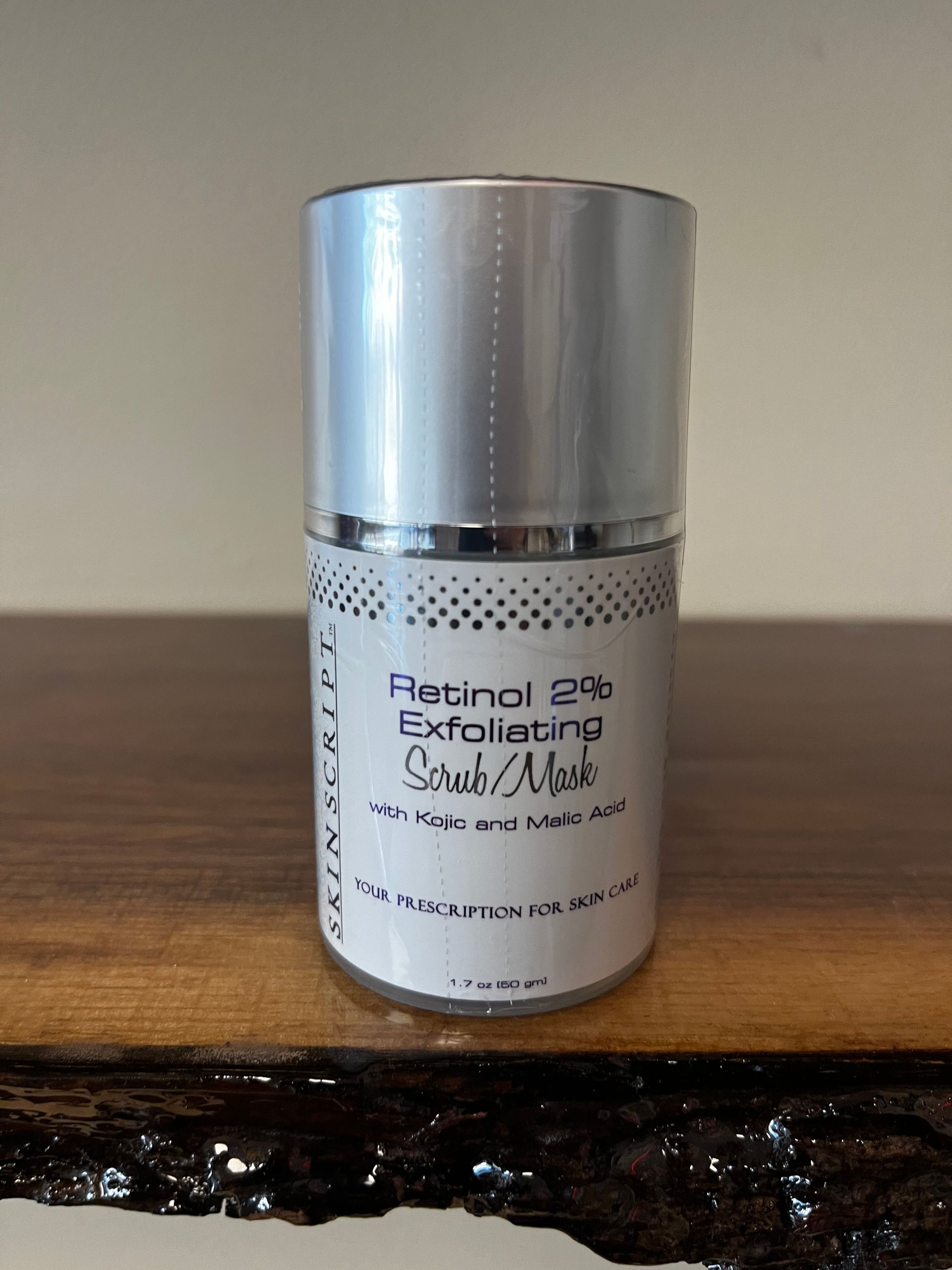 Silver cosmetic bottle labeled “Retinol 2% Exfoliating Serum” on a wooden table