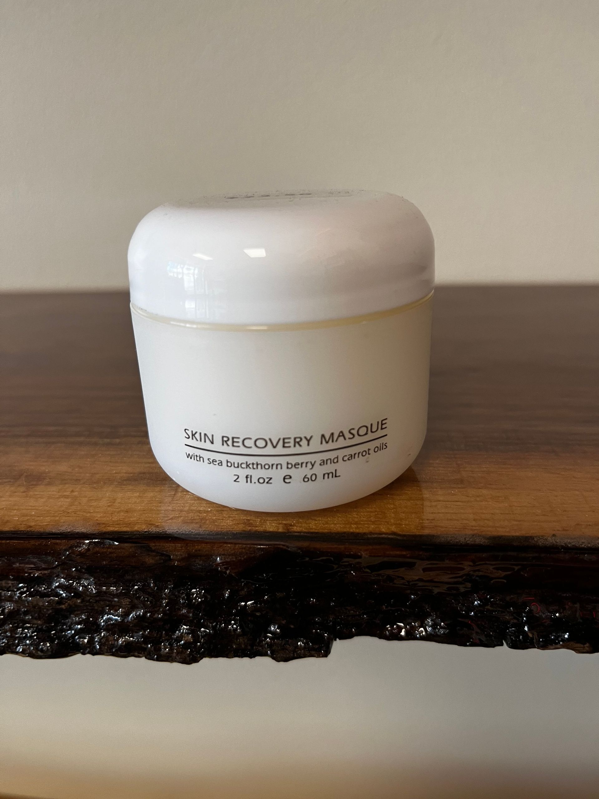 White cosmetic jar labeled “Recovery Mask” on a wooden surface against a plain wall.