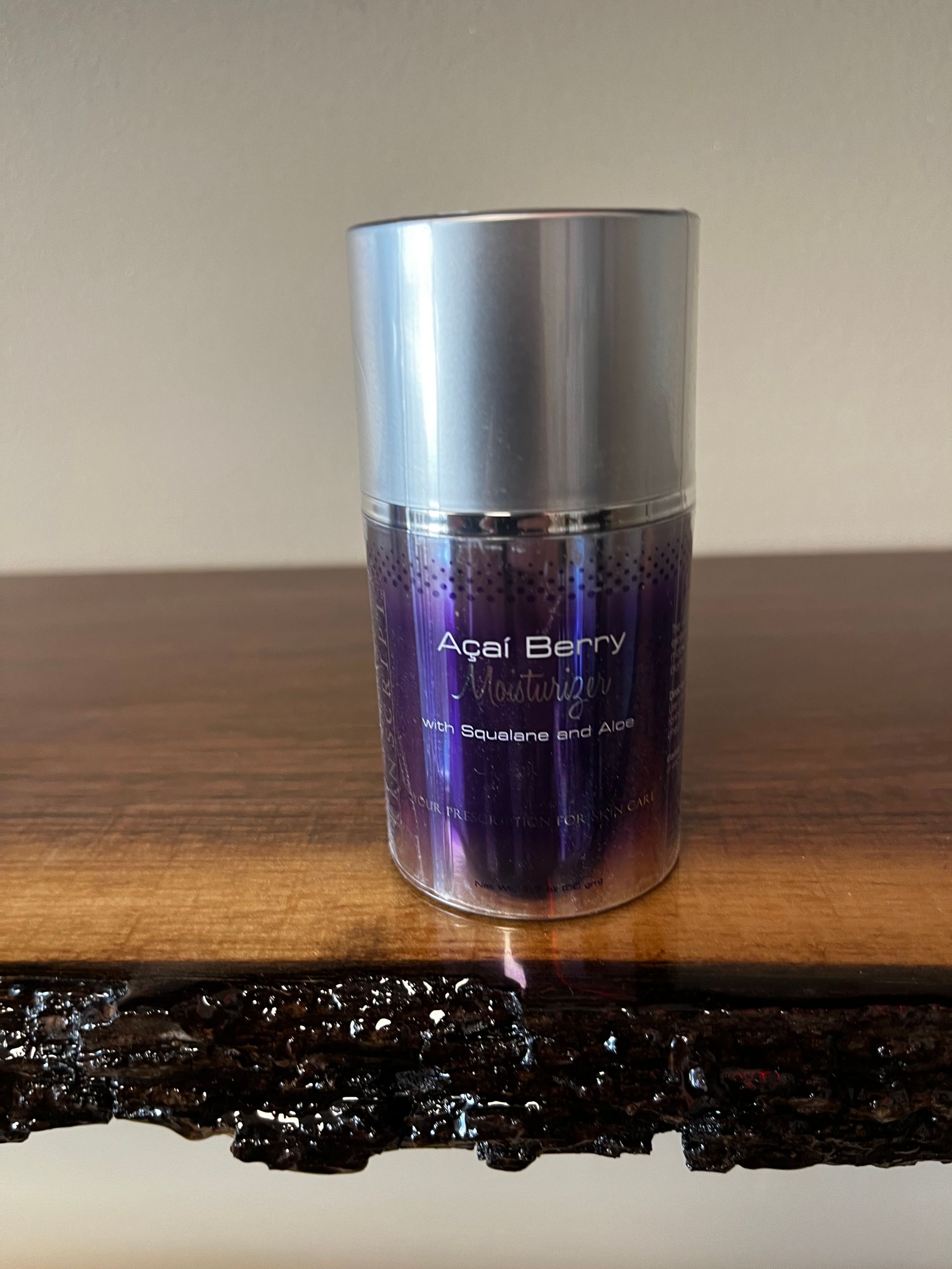 A purple Jo Malone perfume bottle with a silver cap on a wooden table.