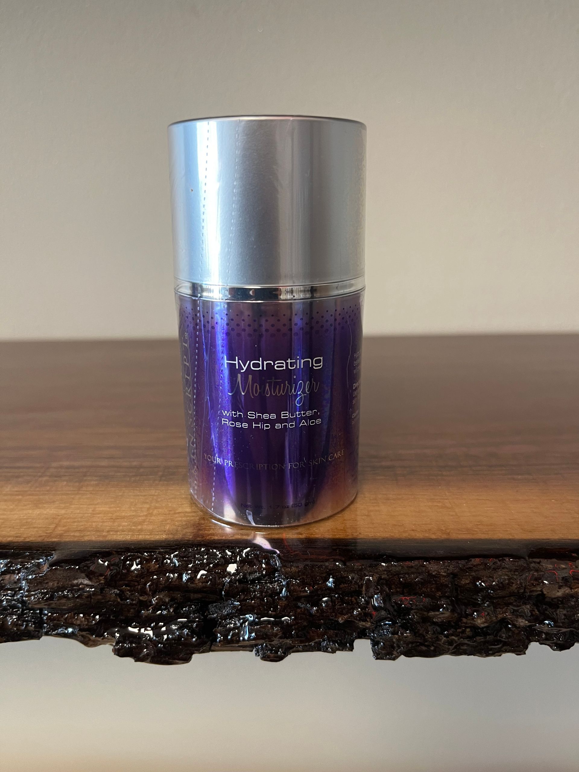 Purple cosmetic bottle with a silver cap sitting on a wooden shelf