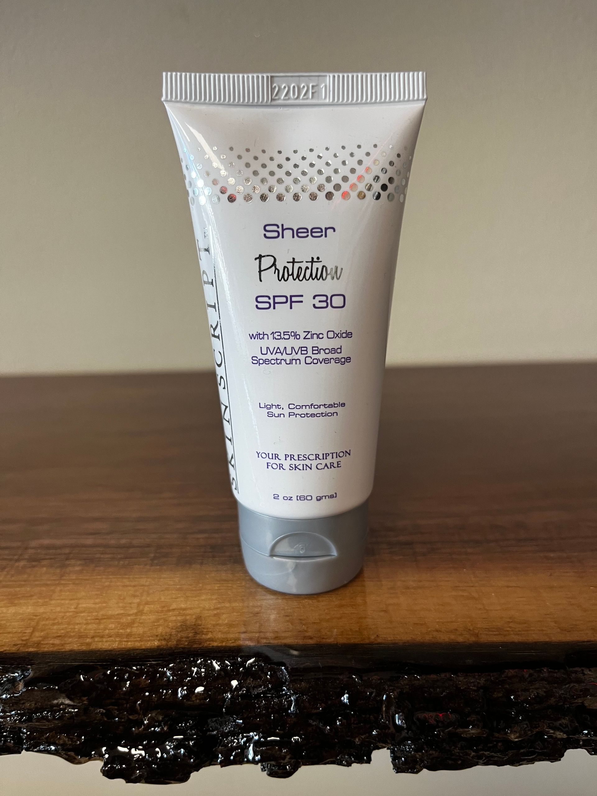White squeeze tube of cream standing on a wooden surface against a plain wall.