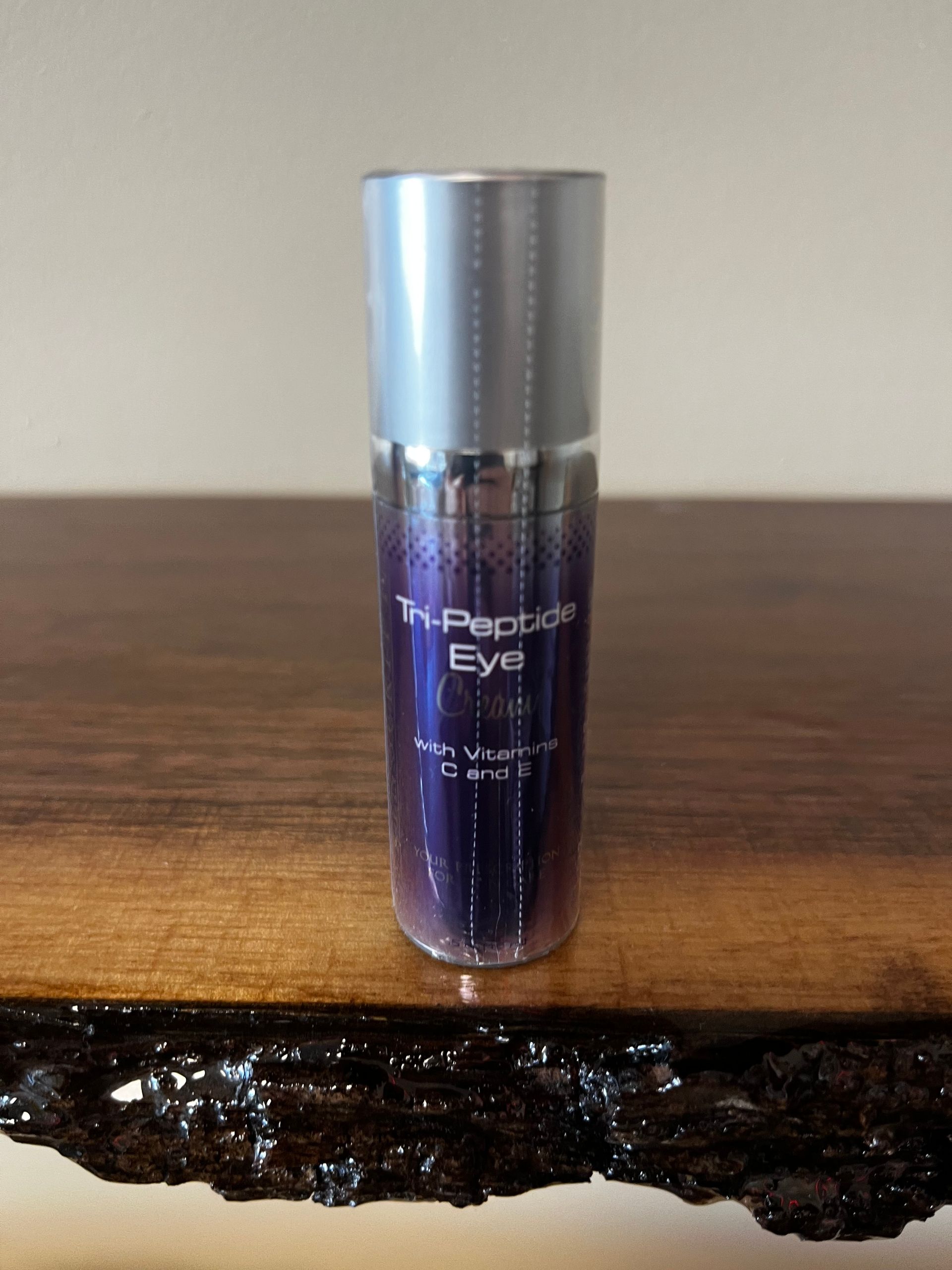 Purple skincare bottle labeled “Eye” standing on a wooden surface against a plain background