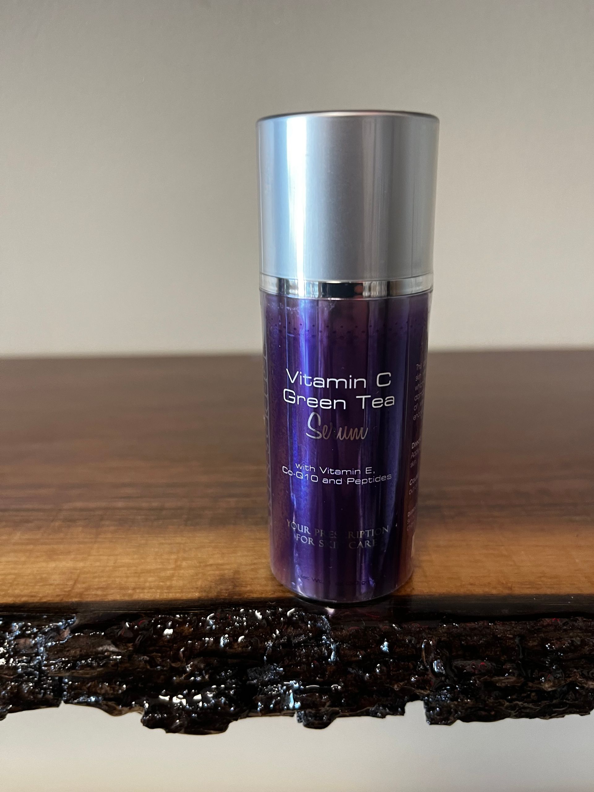 Purple skincare bottle with silver cap standing on a wooden surface against a plain wall