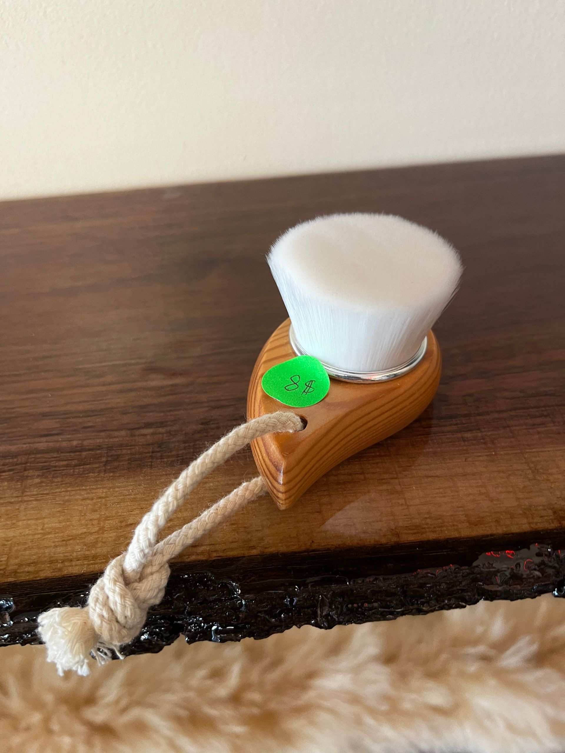 Small white scrub brush with a rope handle resting in a tan holder on a wooden surface.