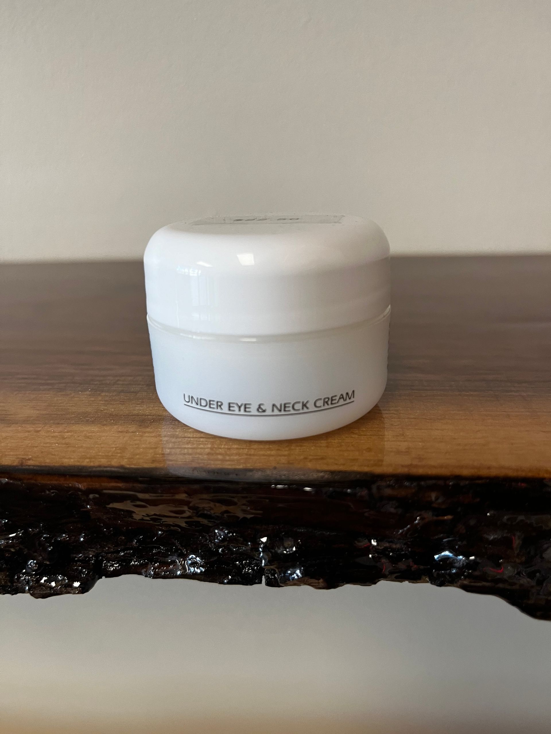 White cream jar on a wooden surface against a plain background.