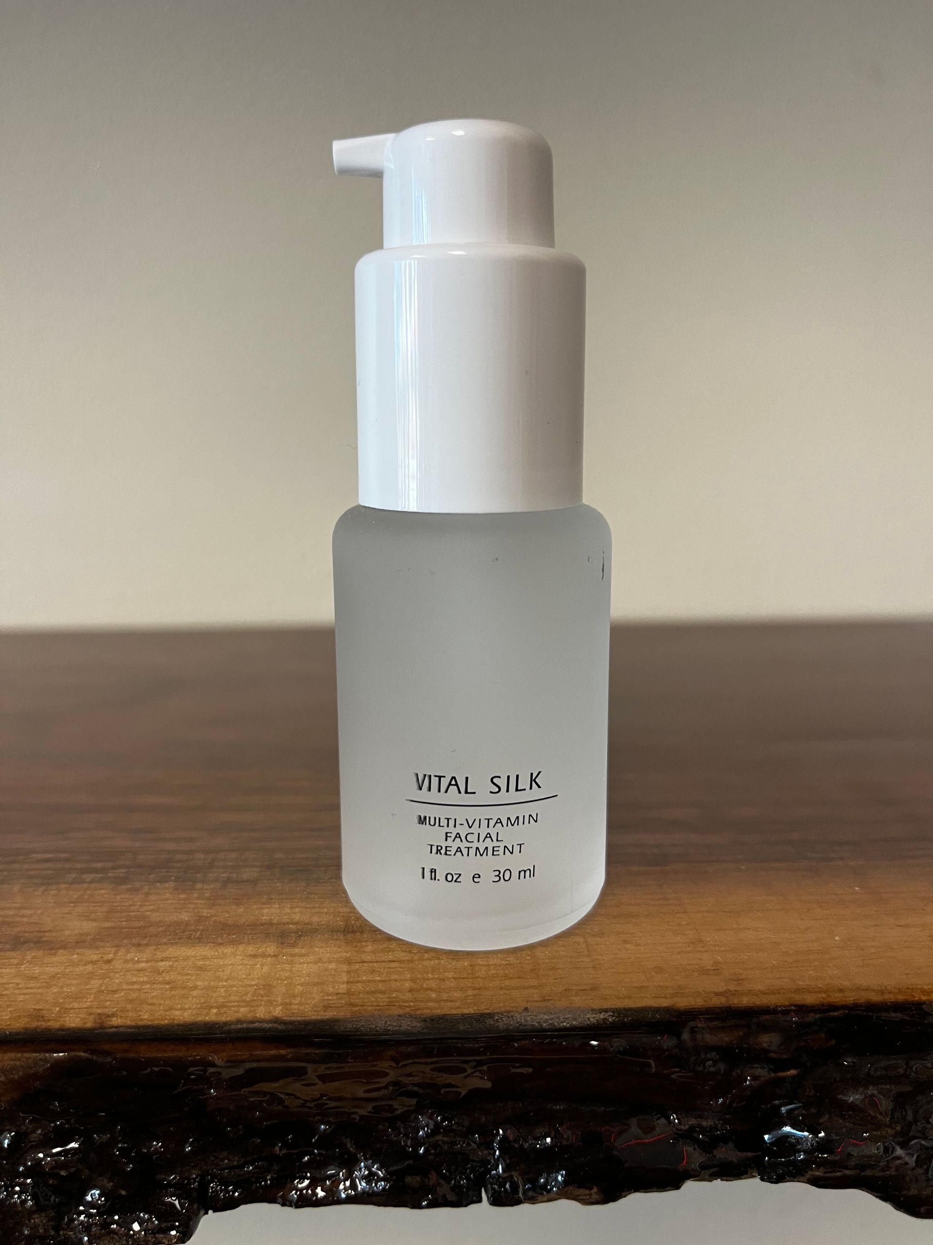 Frosted glass pump bottle on a wooden surface against a plain beige background