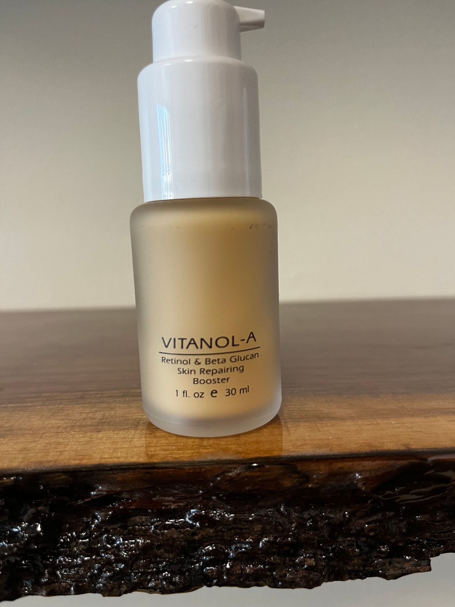 Small frosted skincare bottle with white pump on a wooden surface against a plain wall