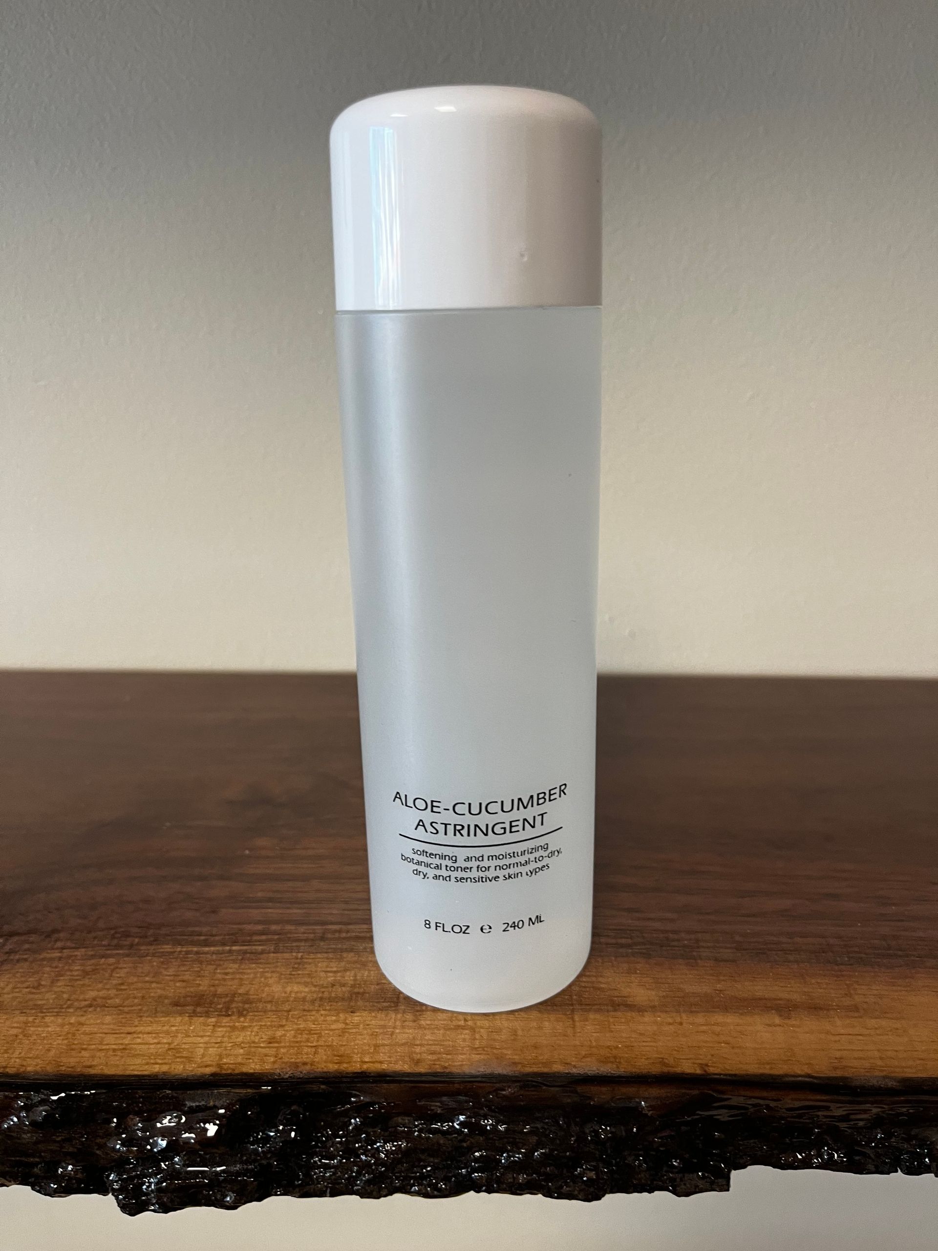 White cylindrical bottle with a white cap standing on a wooden table against a plain wall.