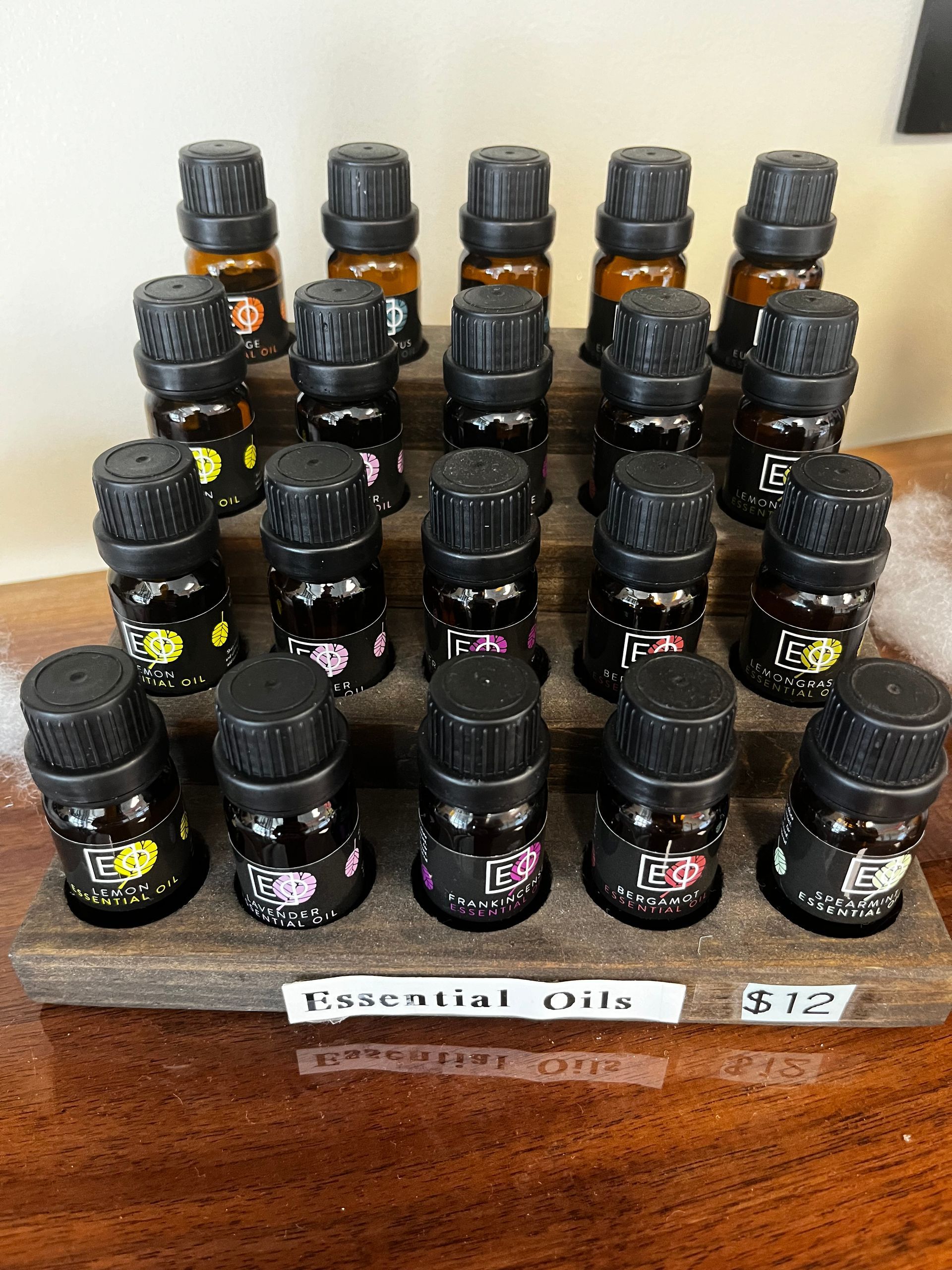 Rows of small black bottles with colorful labels arranged on a shelf, with a handwritten label in front.