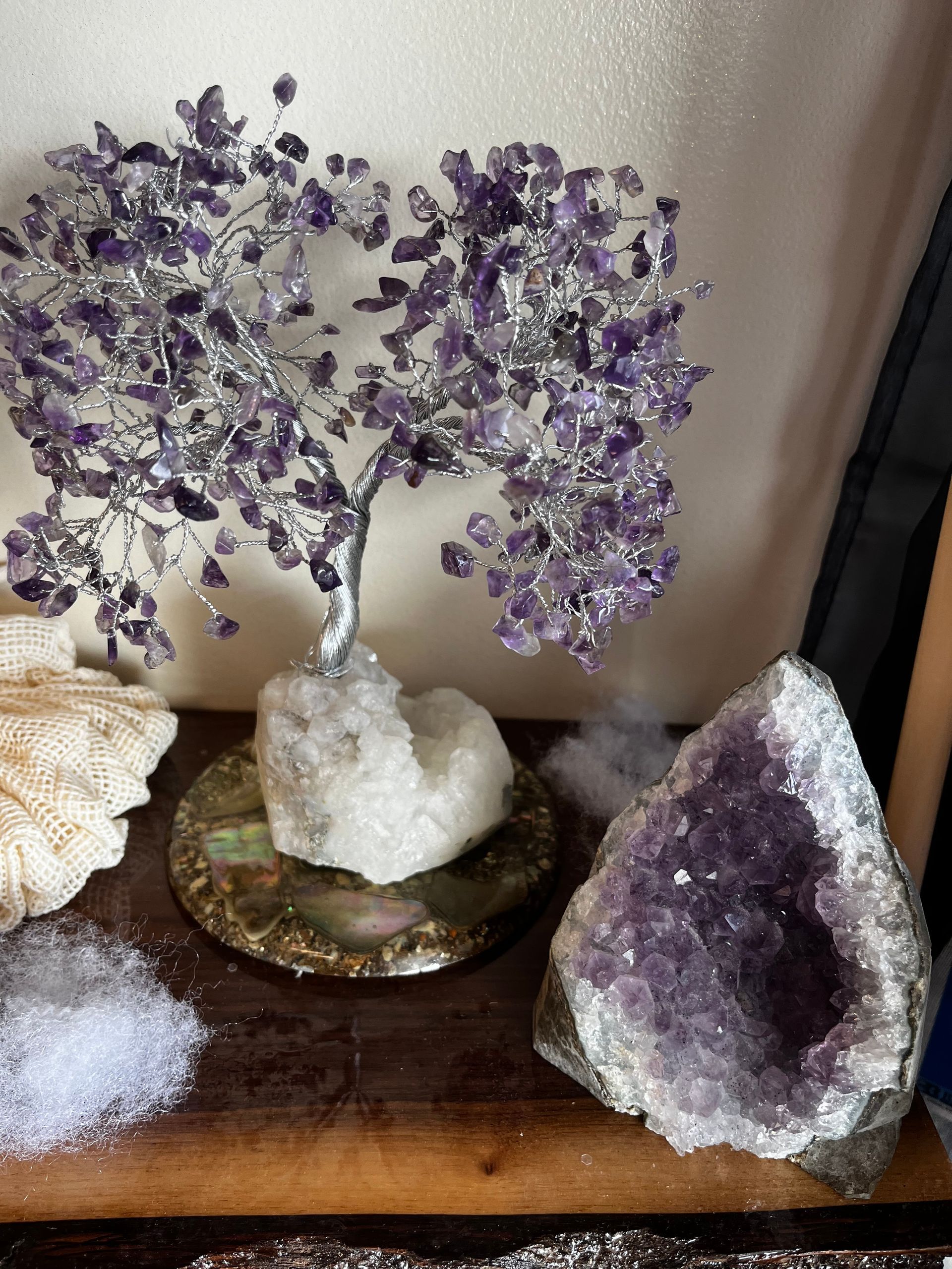Amethyst crystal tree and geodes displayed on a wooden shelf against a beige wall