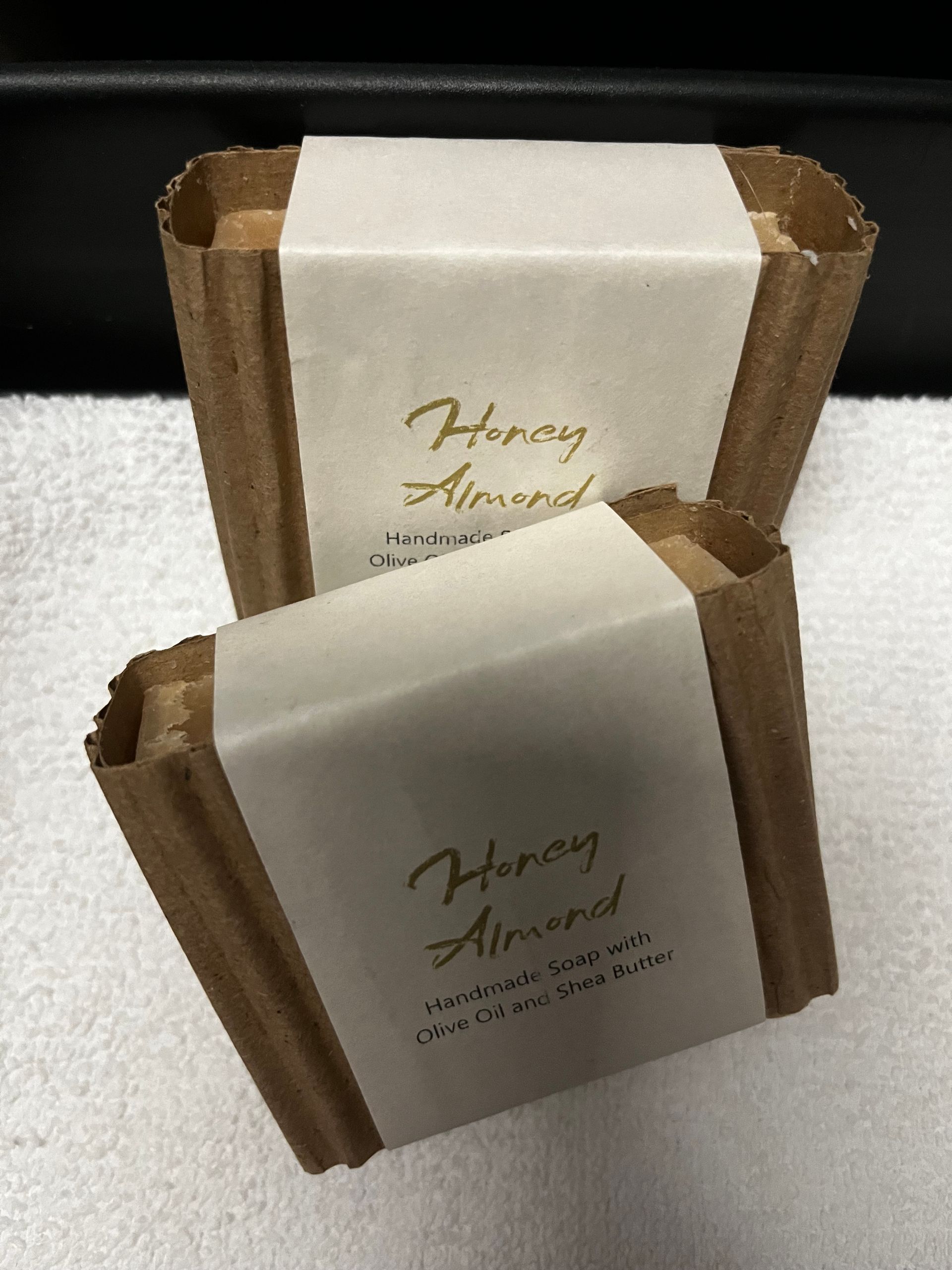 Two brown-and-cream wrapped soap bars with “Honey Almond” labels stacked on a white surface